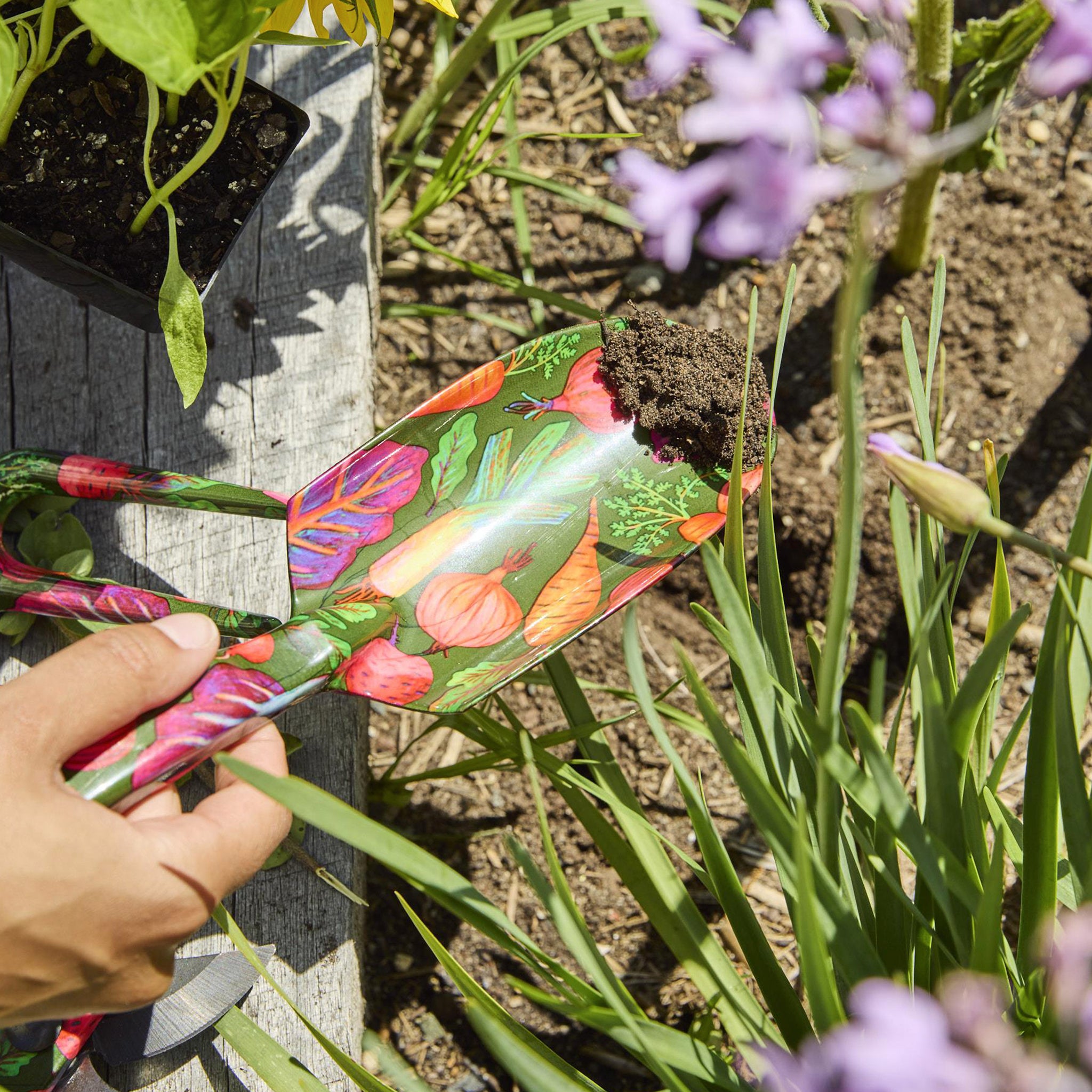 Colorful garden marker with floral design held by a hand in a garden setting.