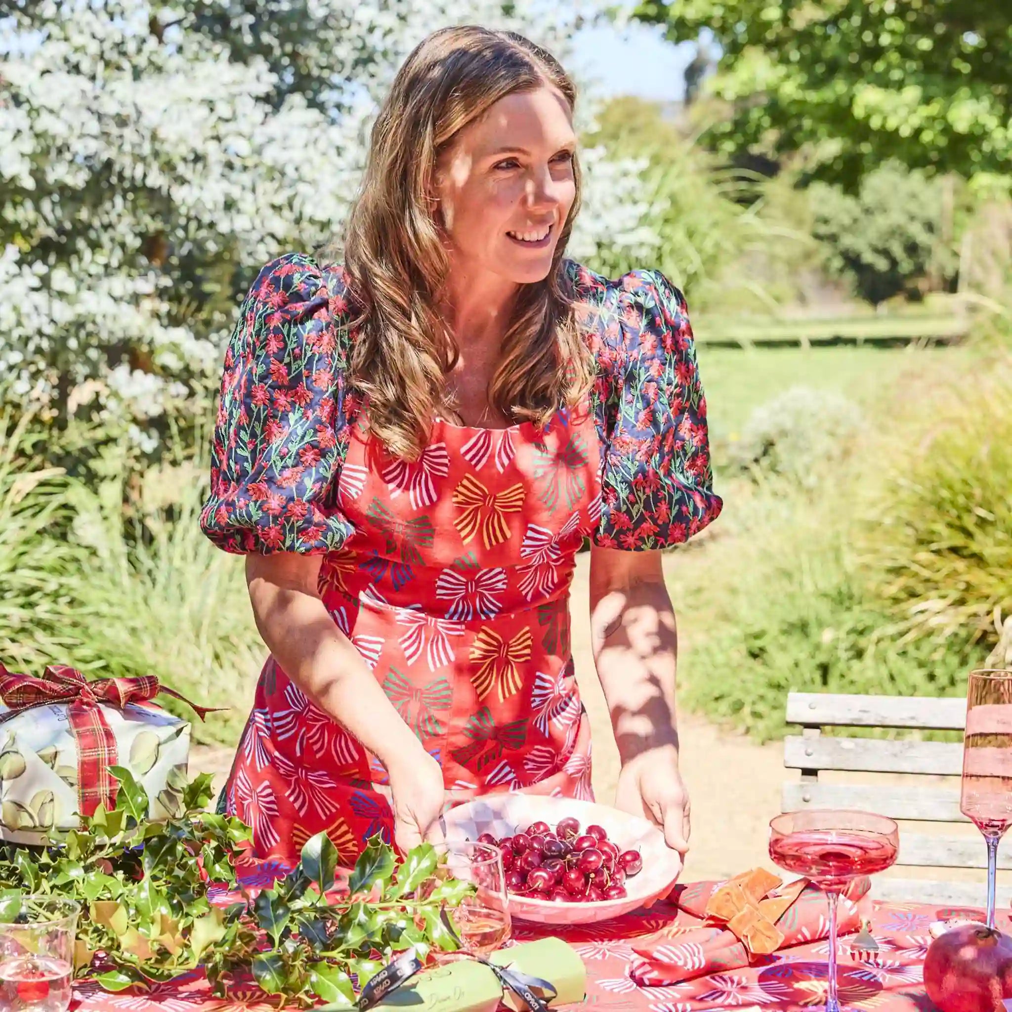 Woman in a garden setting, preparing food at a table with a floral dress.