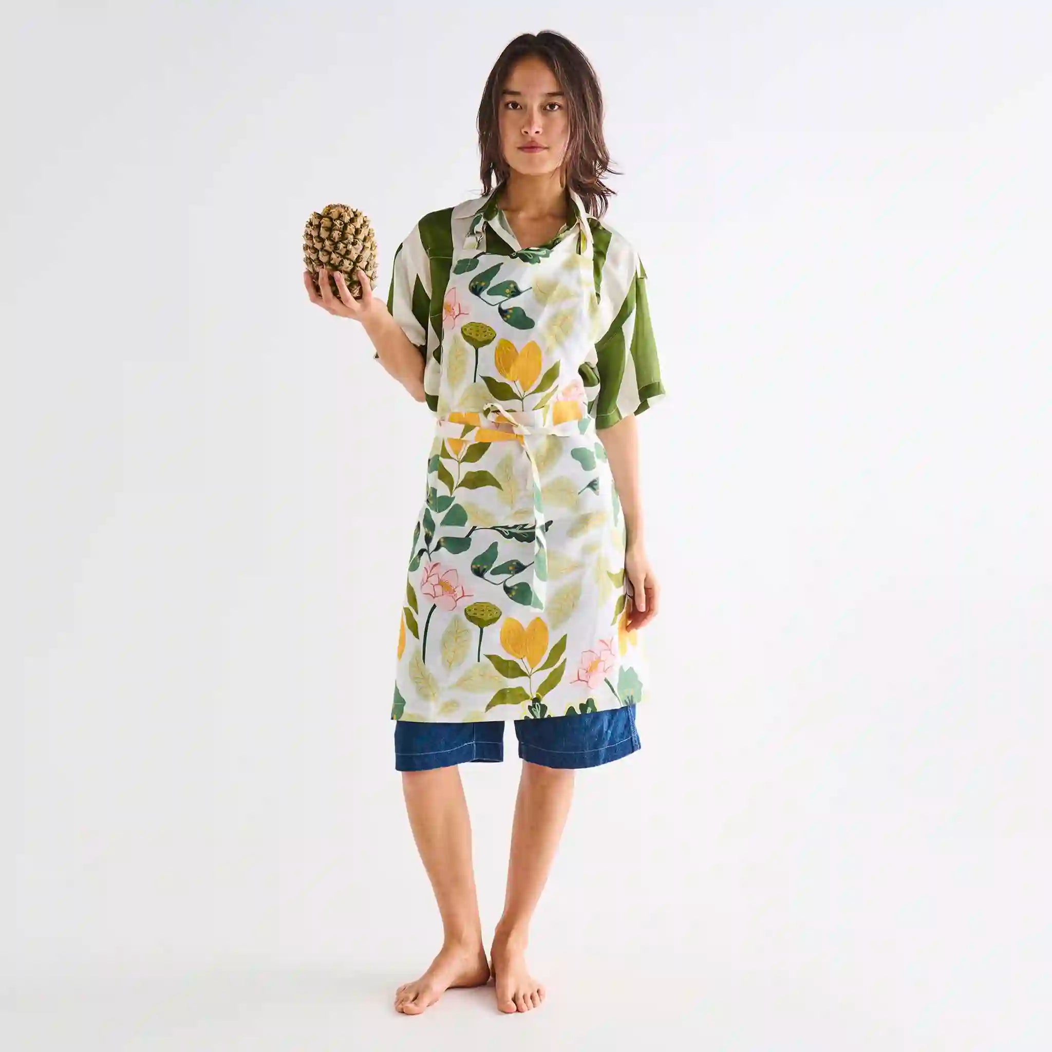 Woman wearing a floral apron holding a pineapple on a white background