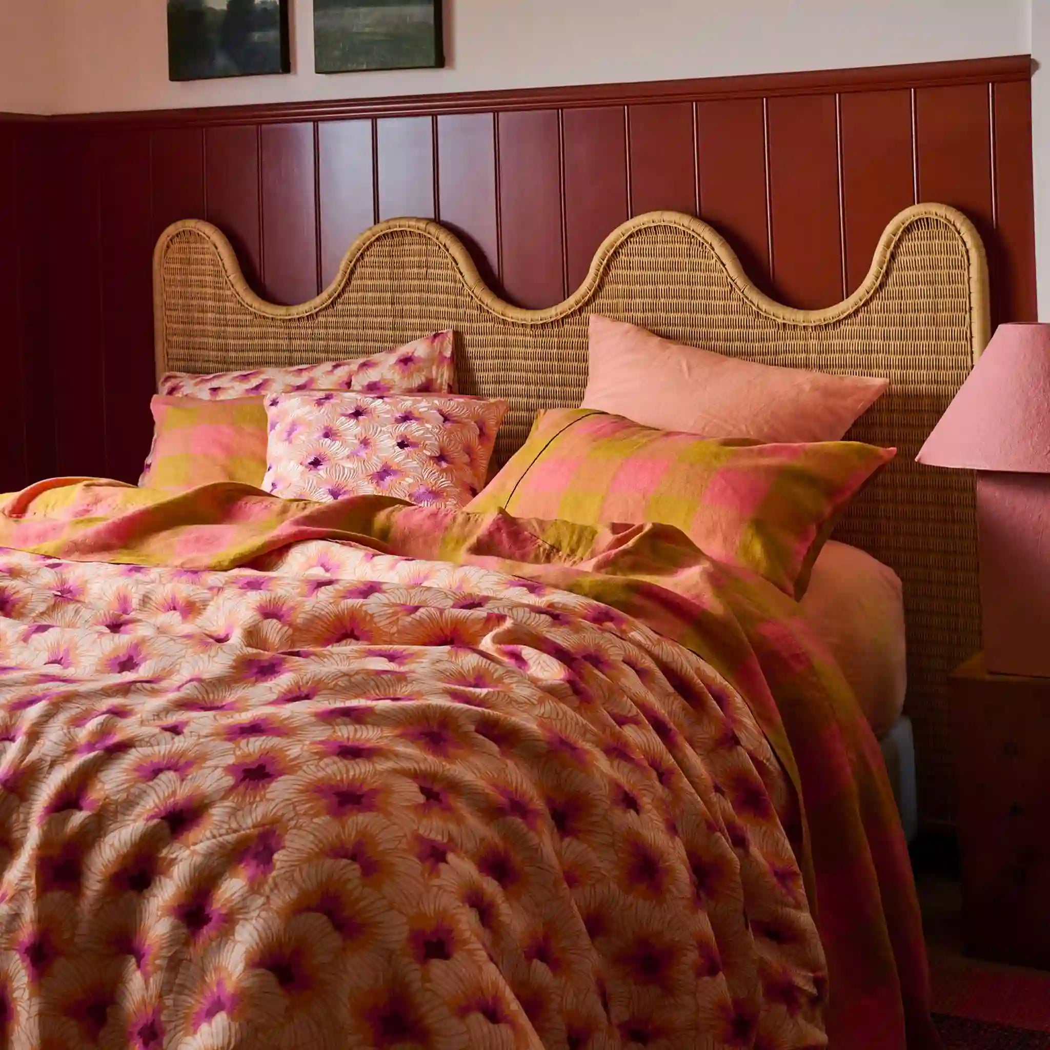 Bed with floral bedding and pink pillows against a wooden headboard.