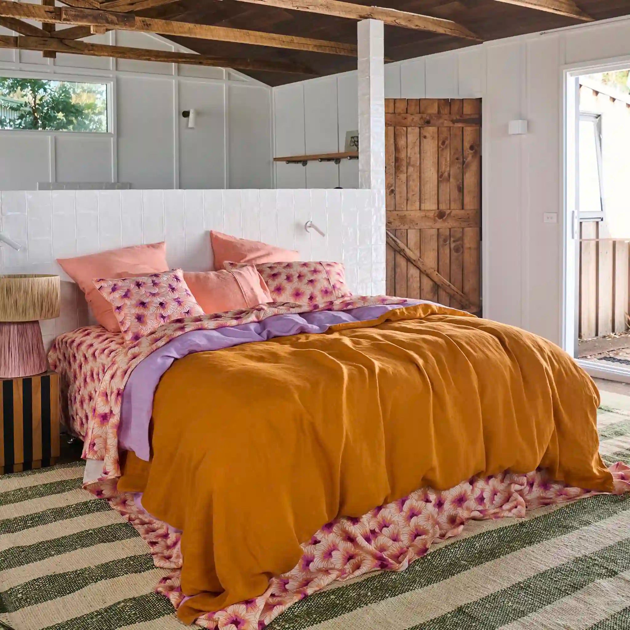 Bedroom with mustard yellow comforter and pink floral pillows on a striped rug.