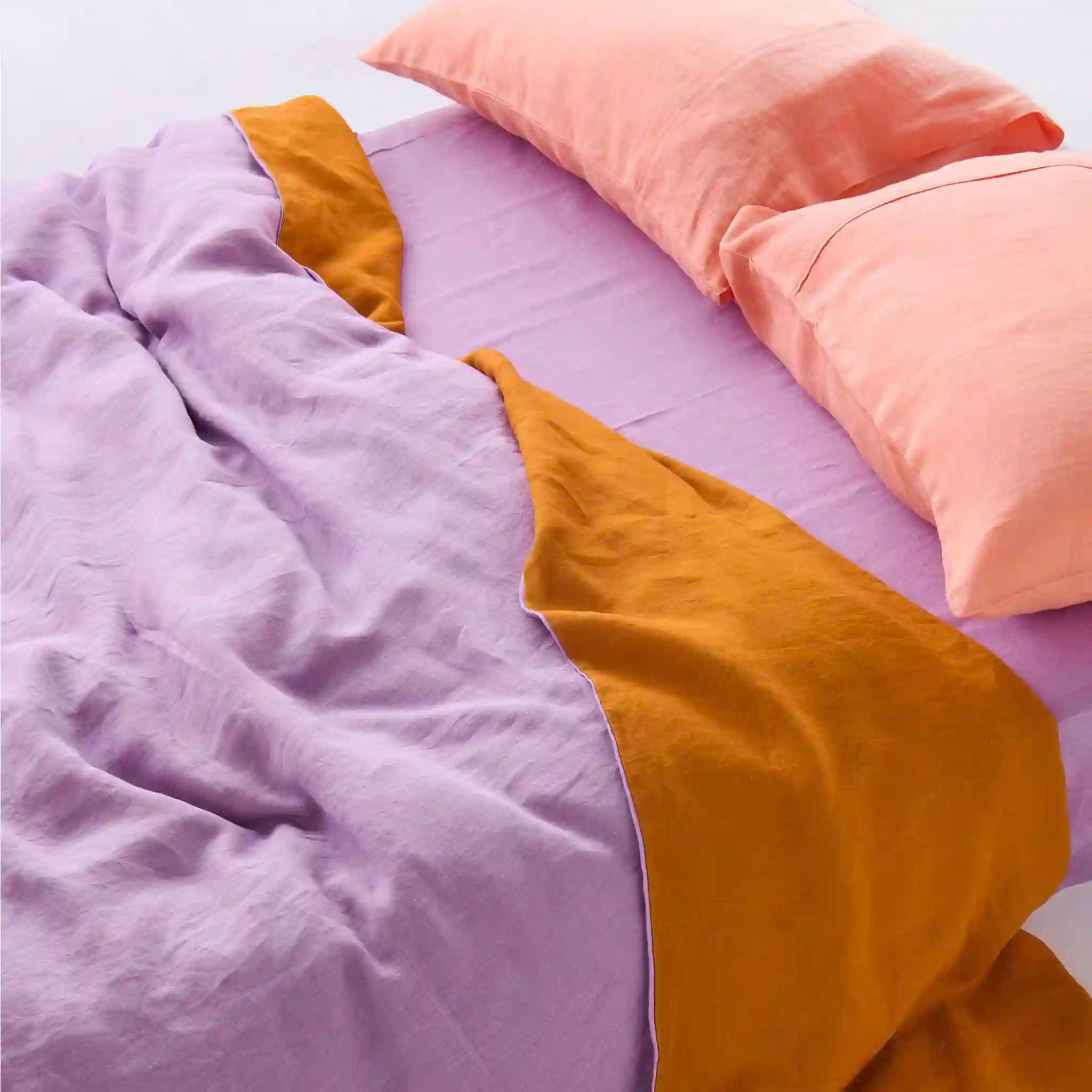 Purple and mustard-colored bedding with pink pillows on a bed.