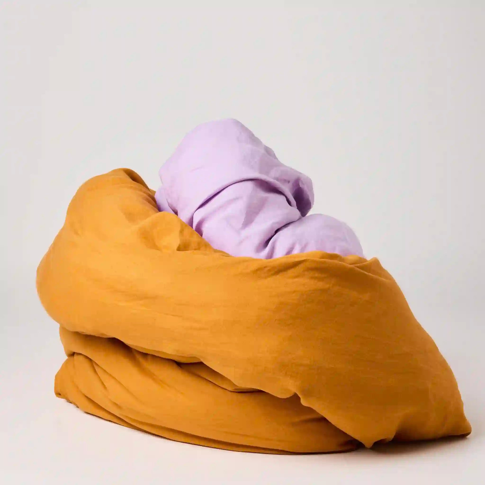 Folded mustard yellow blanket and purple garment on a light gray background