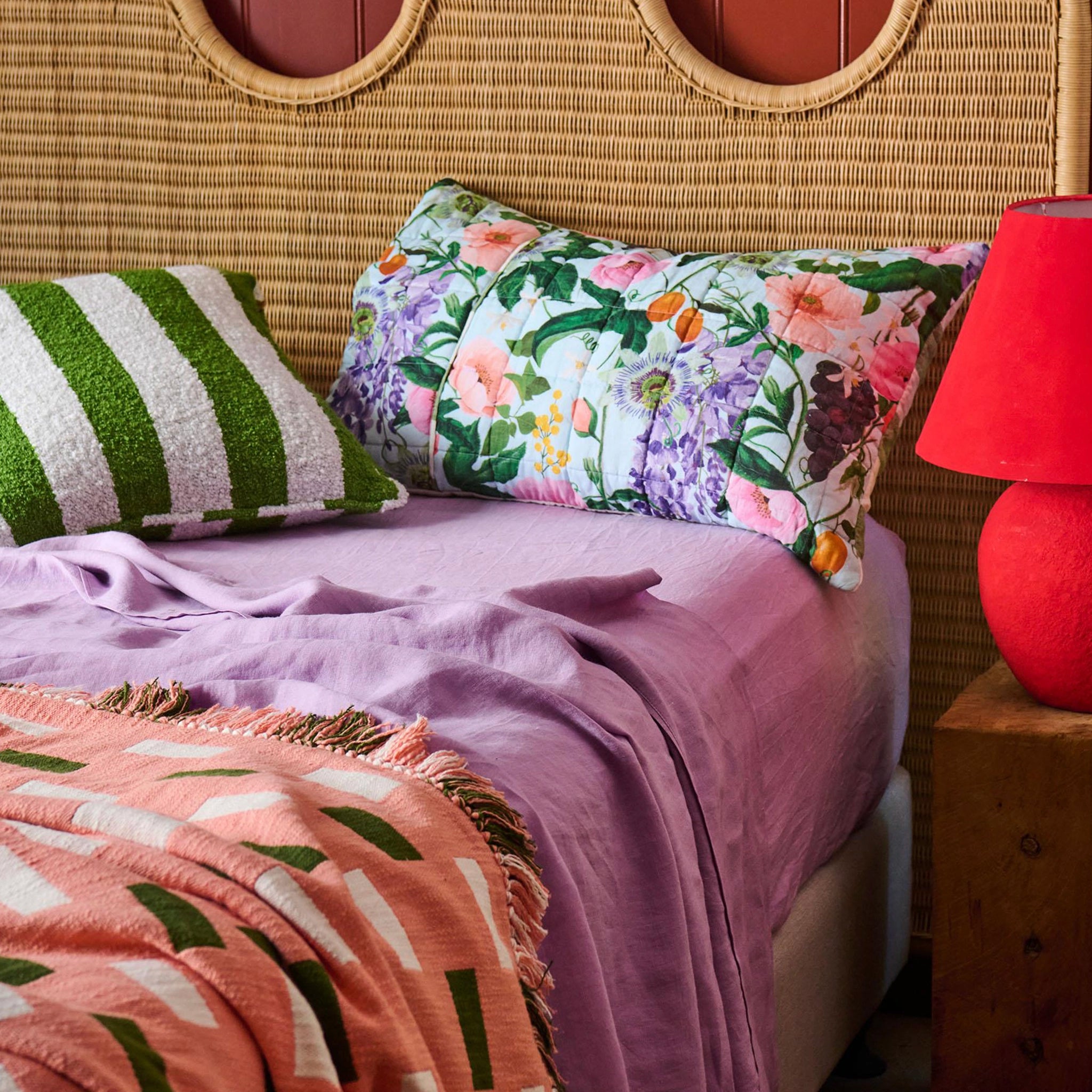 Bed with floral pillow, striped pillow, and pink blanket against a wicker headboard.