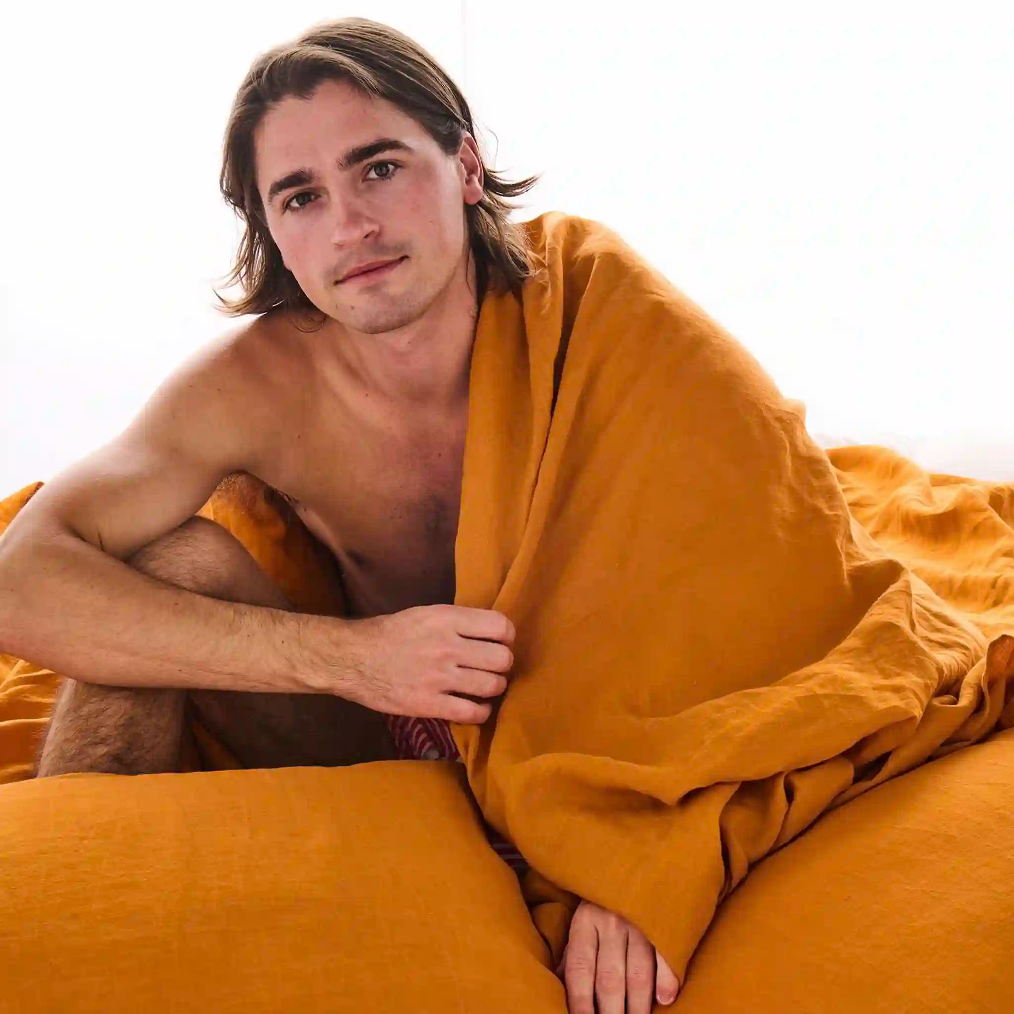 Man wrapped in a mustard yellow flat sheet on a white background