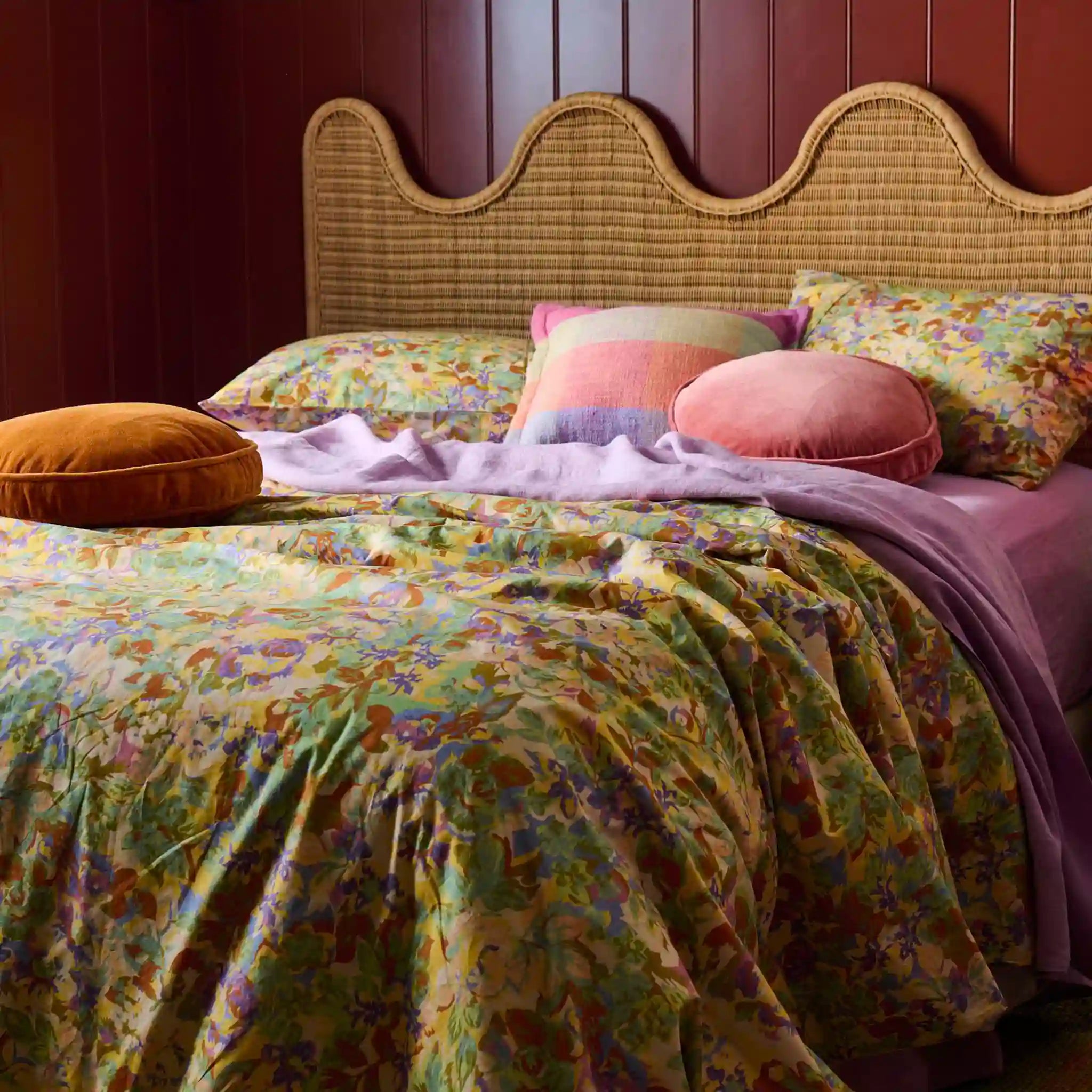 Bed with floral bedding and colorful pillows against a wooden panel wall.