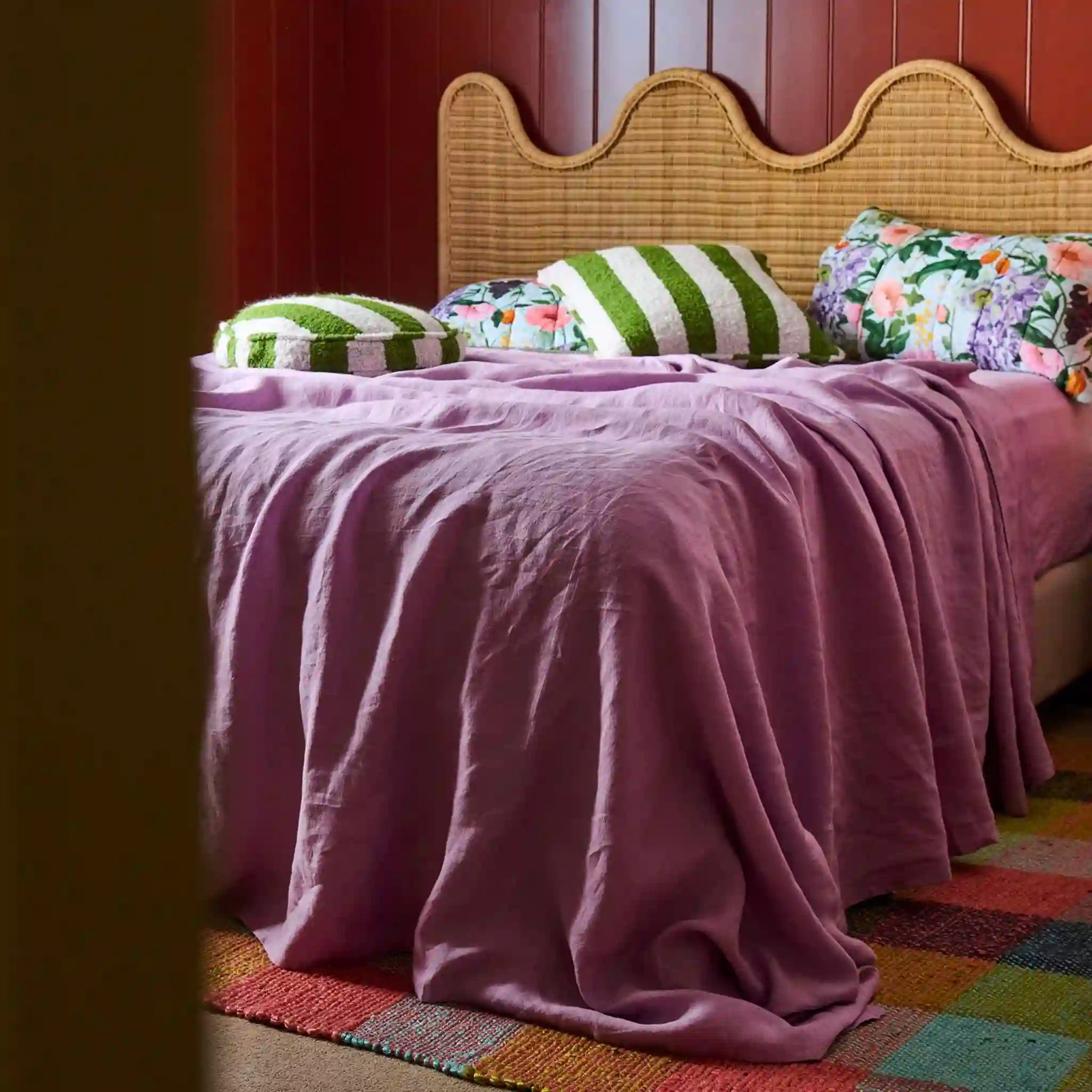Bed with pink bedding and colorful pillows against a wooden paneled wall.