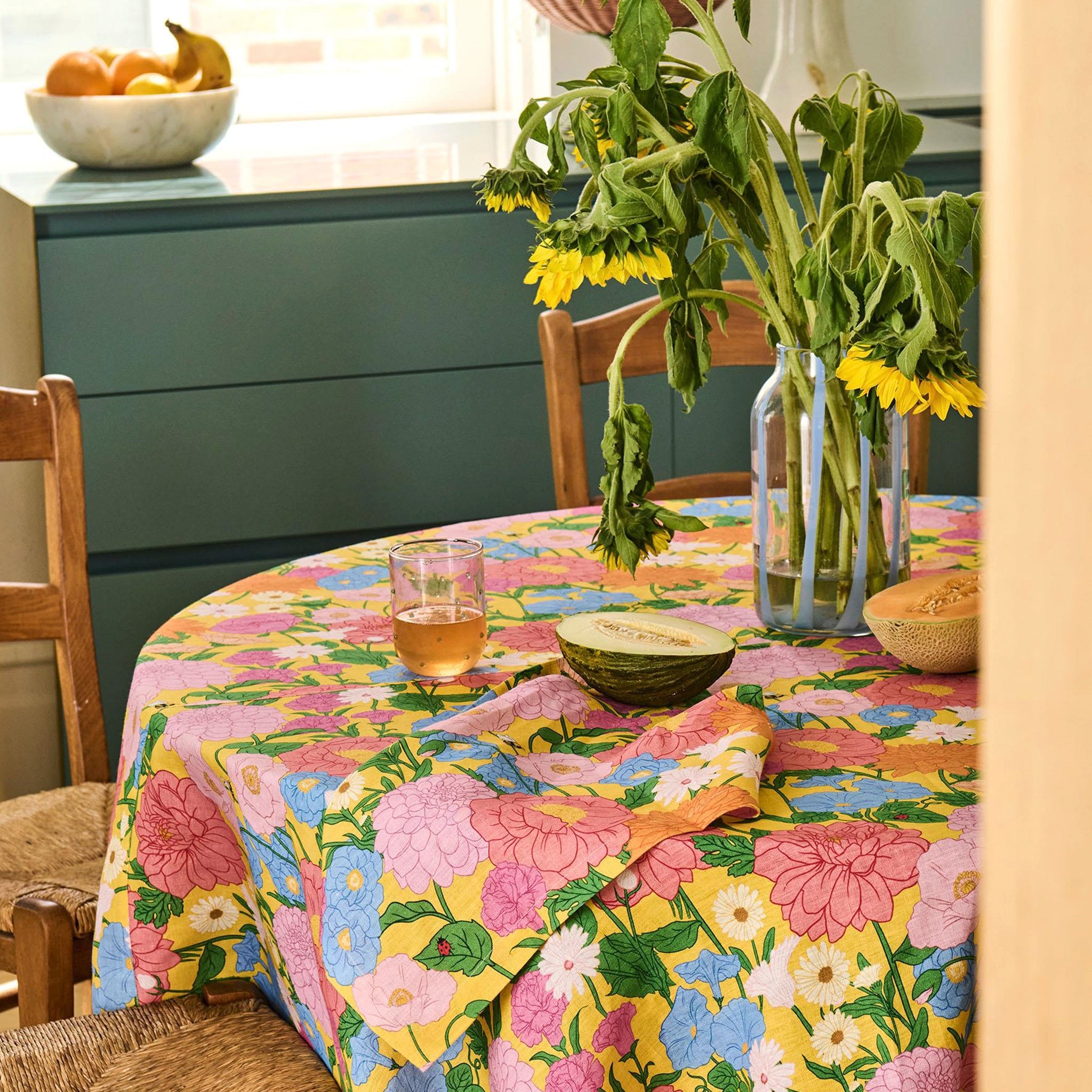 Dining table with a floral tablecloth, glasses, and a vase of sunflowers.