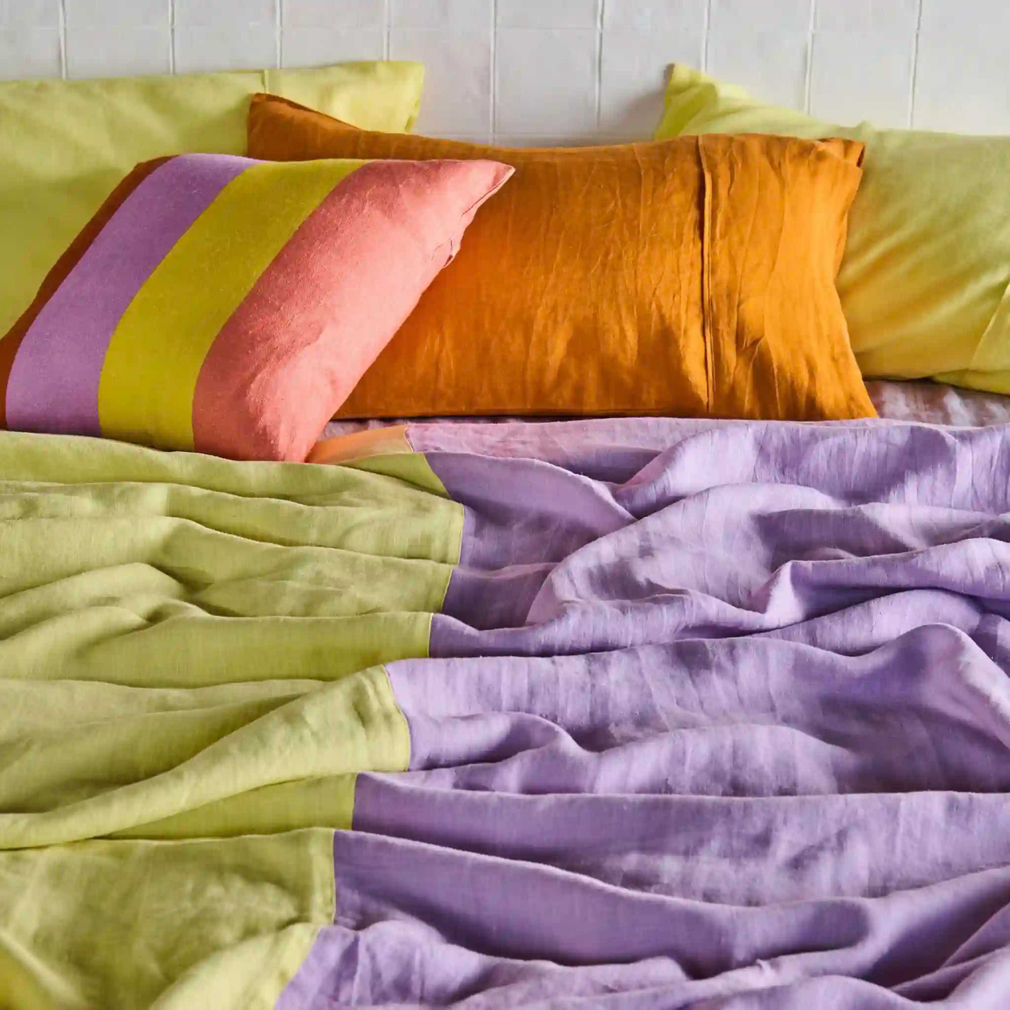 Colorful bedding with green, purple, and orange pillows on a bed.