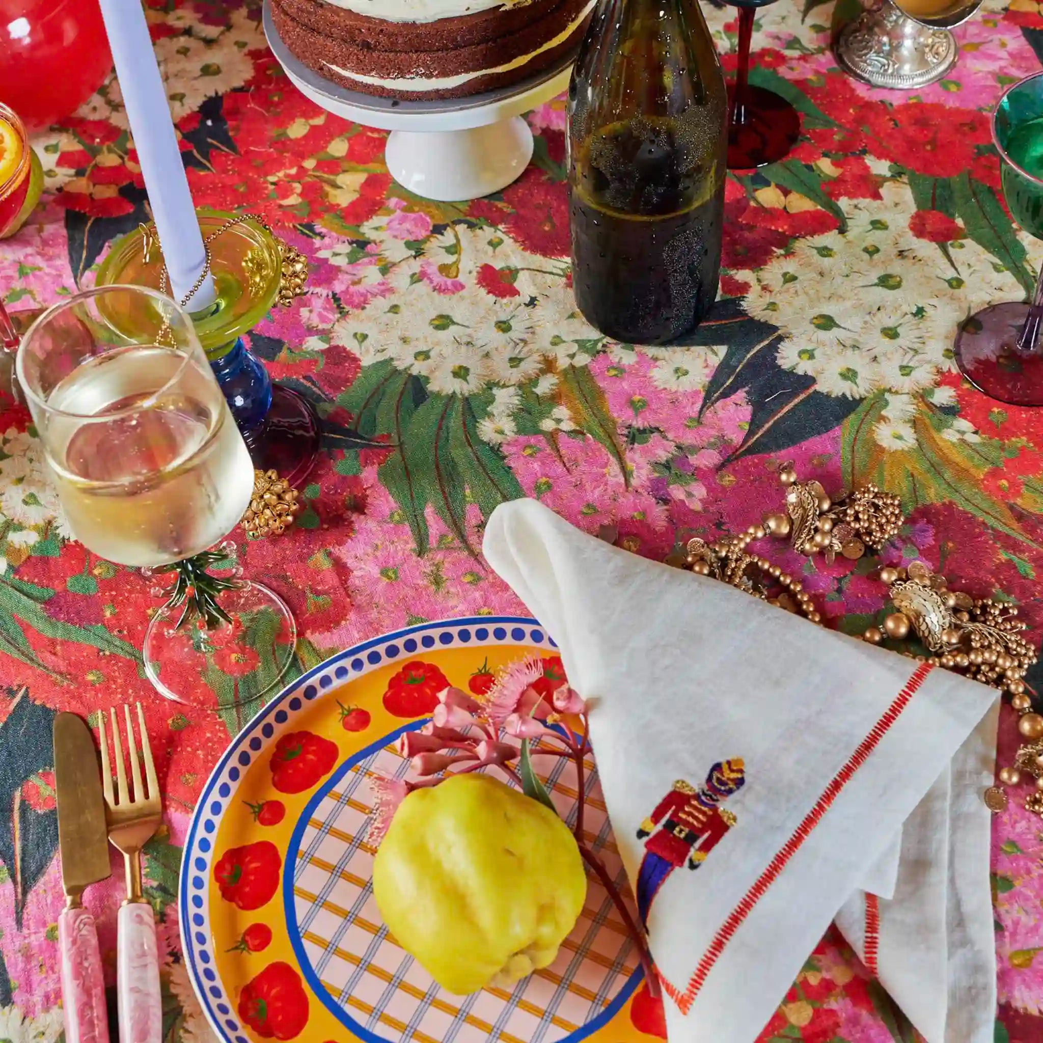 Dessert table setting with a cake, wine, and colorful plates on a patterned tablecloth.