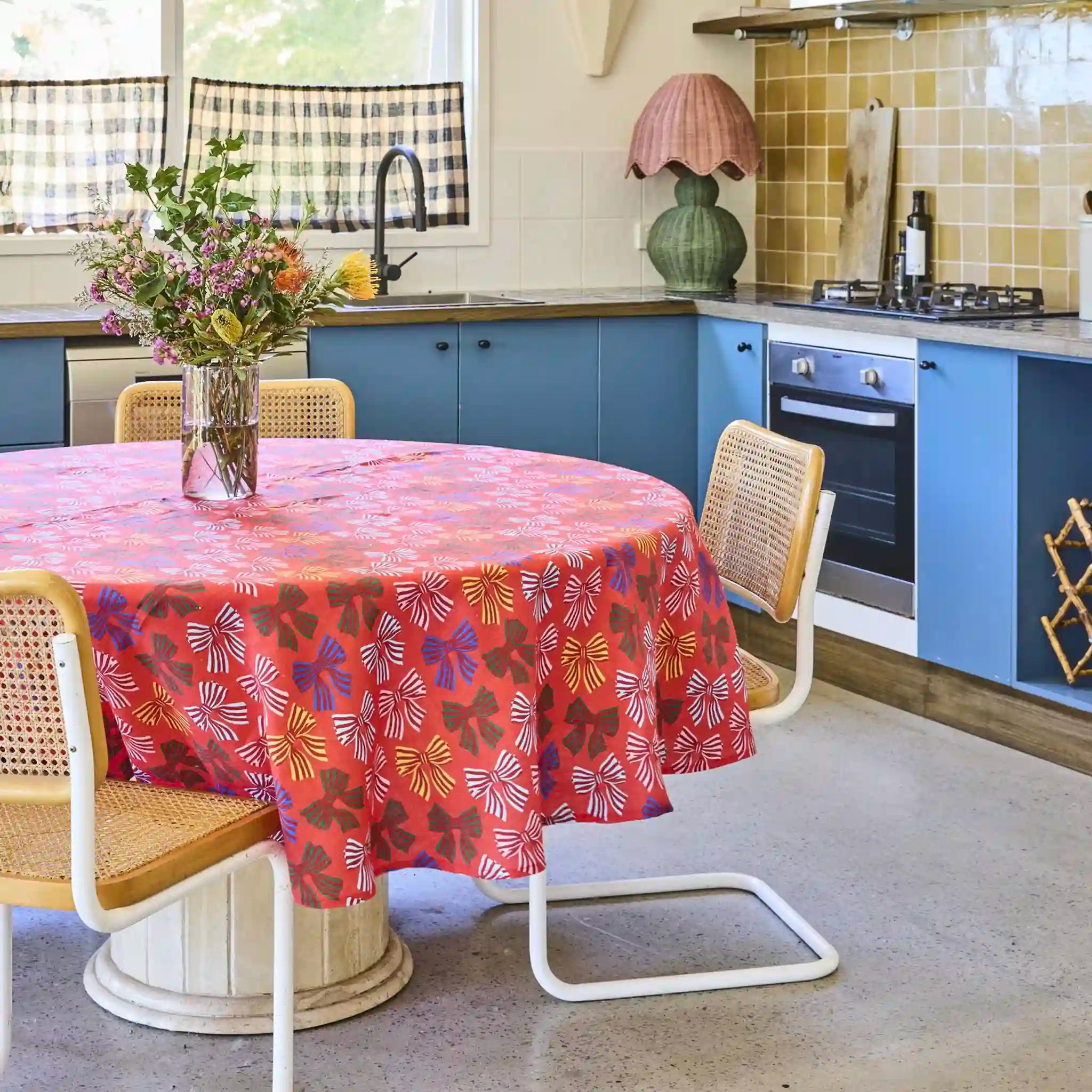 Kitchen with a round table covered by a colorful tablecloth, surrounded by chairs.