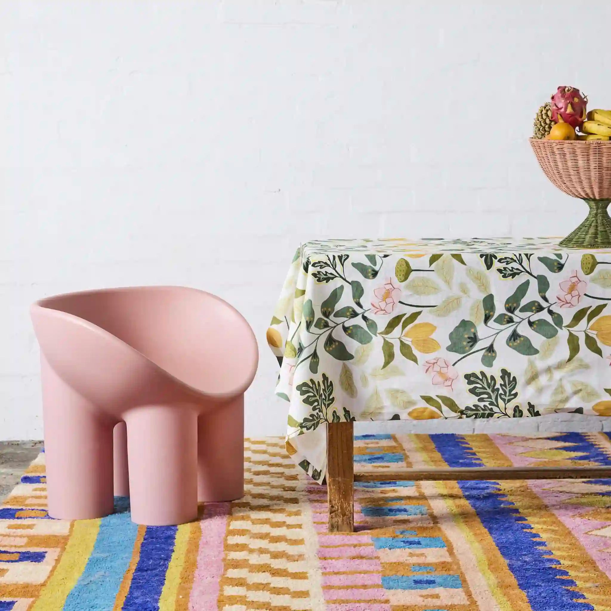 Pink chair and table with floral tablecloth on a colorful rug against a white wall