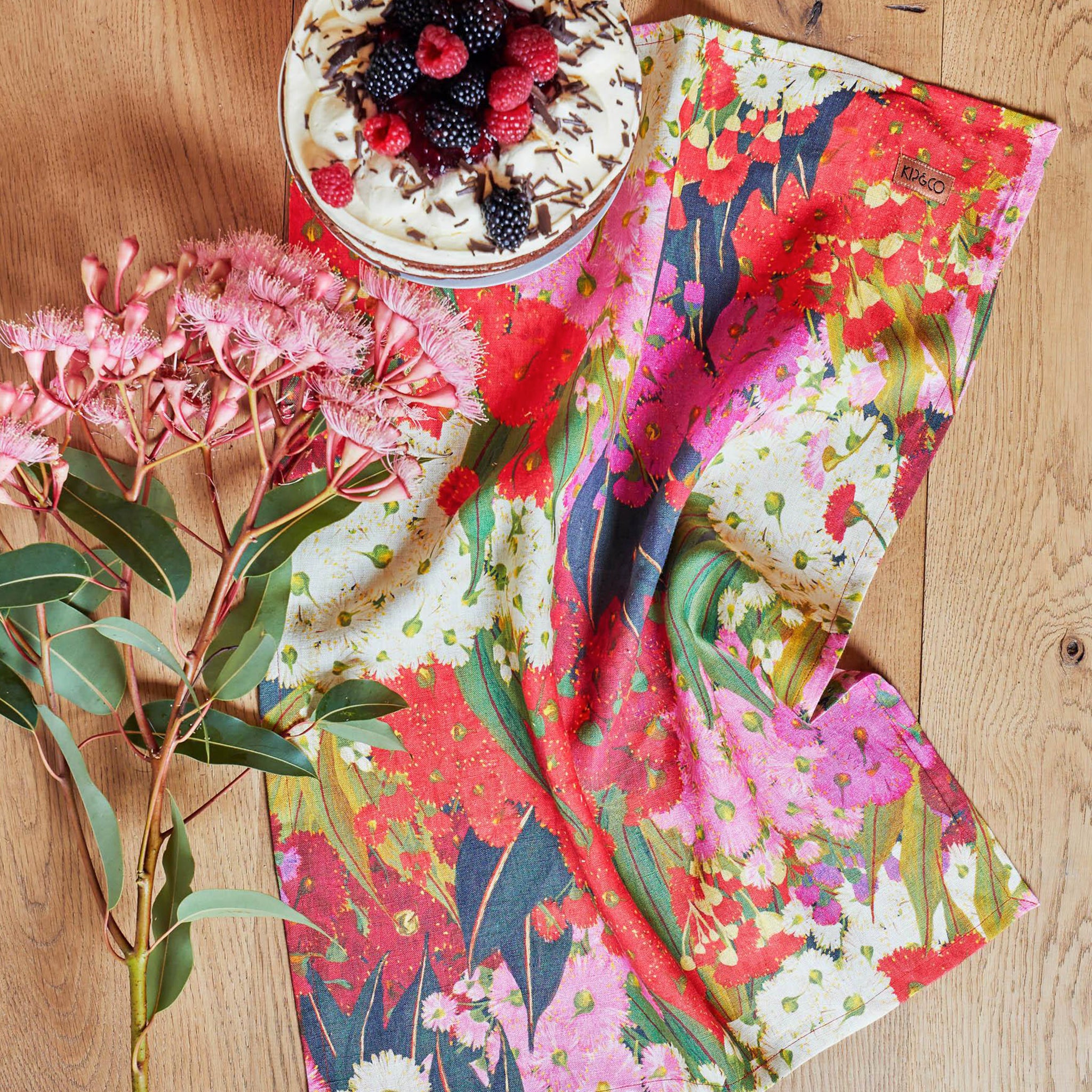 A folded linen tablecloth with a floral pattern featuring rich pinks, reds, and creamy white colors.