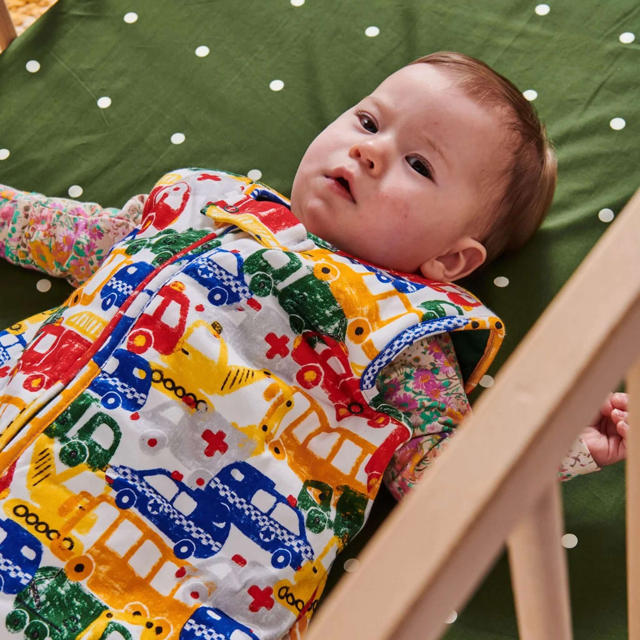 Kip & Co Organic Cotton Baby Fitted Cot Sheet - Polka Dot Cactus on cot mattress with baby lying on green polka dot sheet