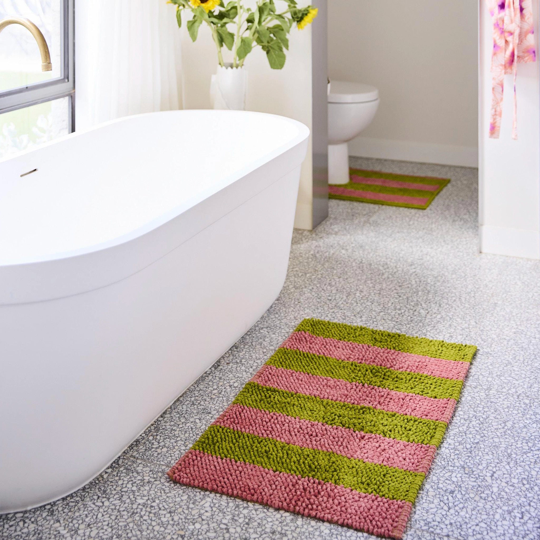 Bathroom with a striped pink and green rug, white bathtub, and toilet.