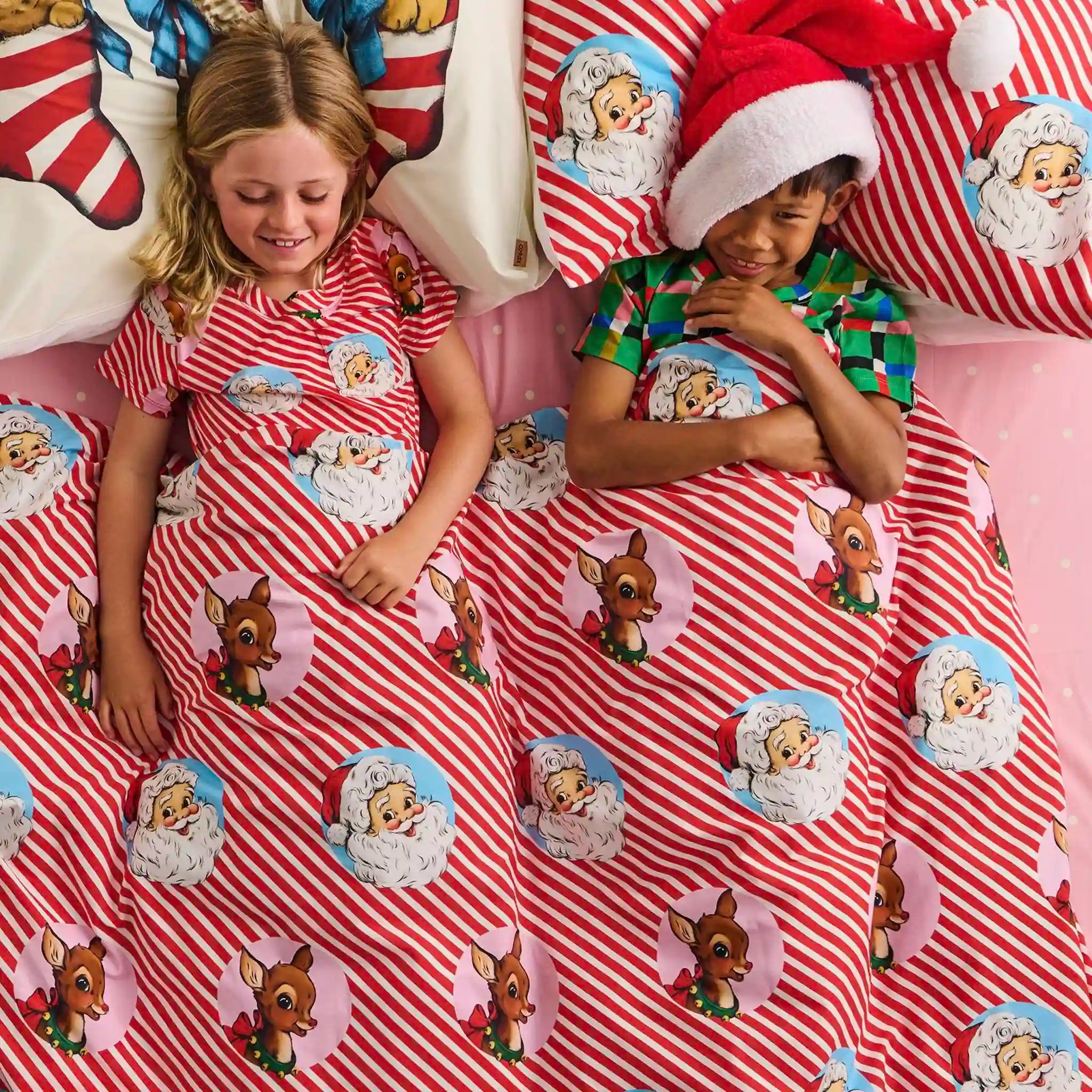 Children in matching Christmas-themed pajamas on a bed with festive bedding.