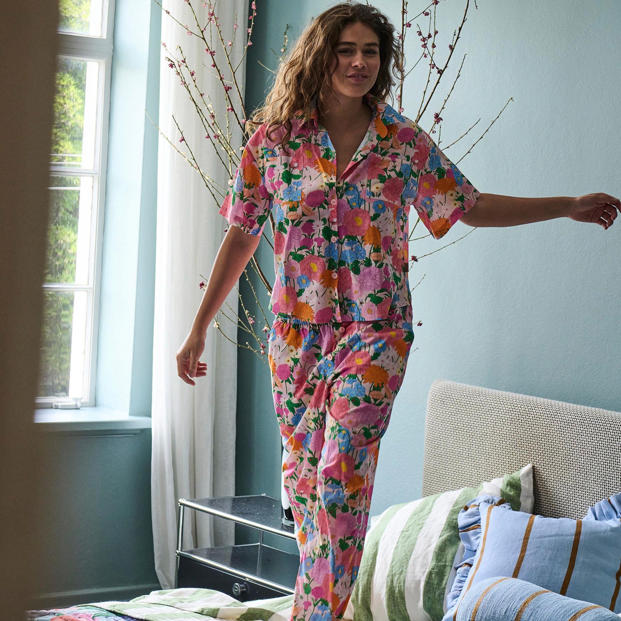 Woman wearing a colorful floral pajama set in a bedroom.