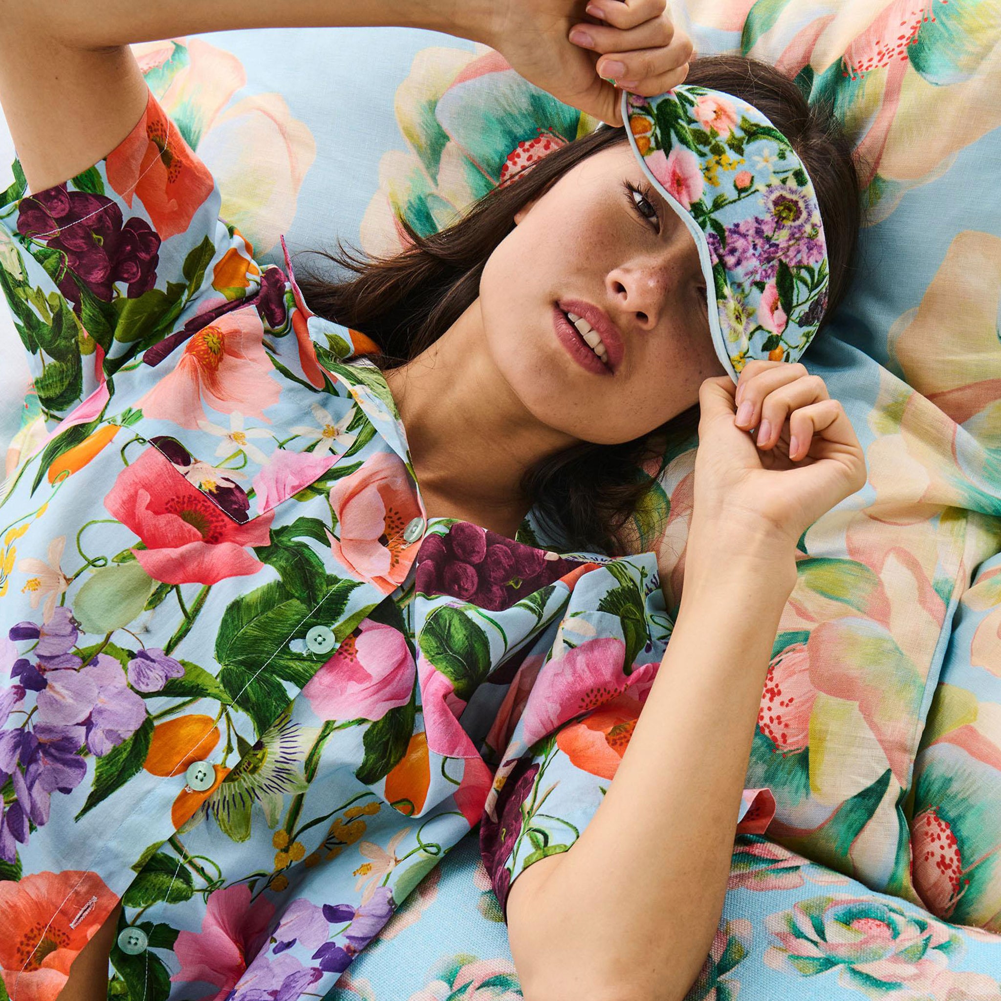 Woman wearing a floral robe and matching headband, lying on a floral-patterned bed.