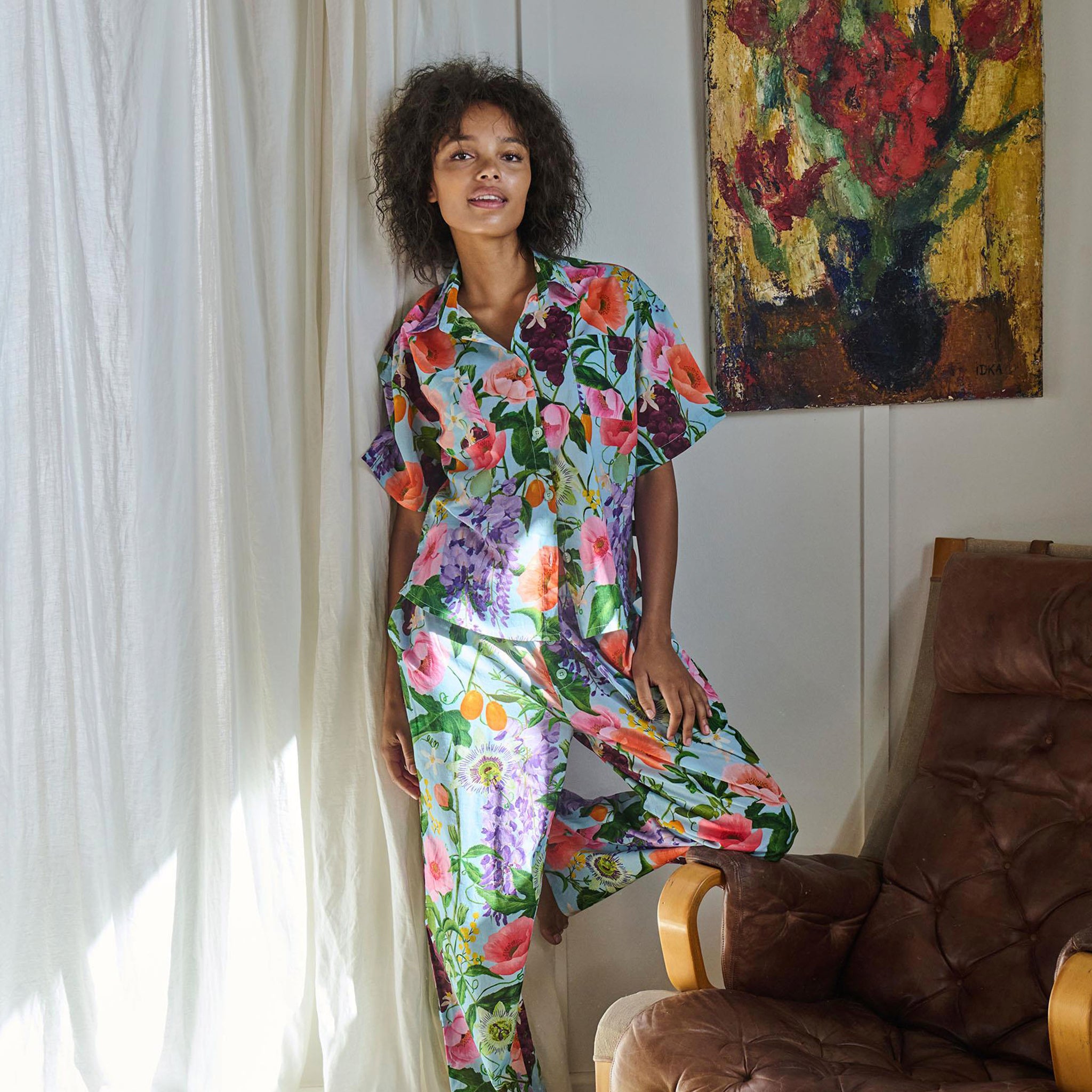 Woman wearing a colorful floral dress standing in a room with a painting on the wall.