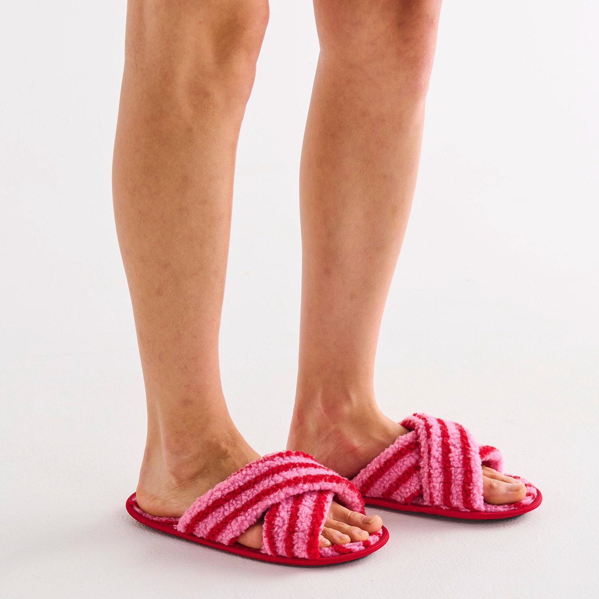 Pink and red striped slippers worn by a person on a white background