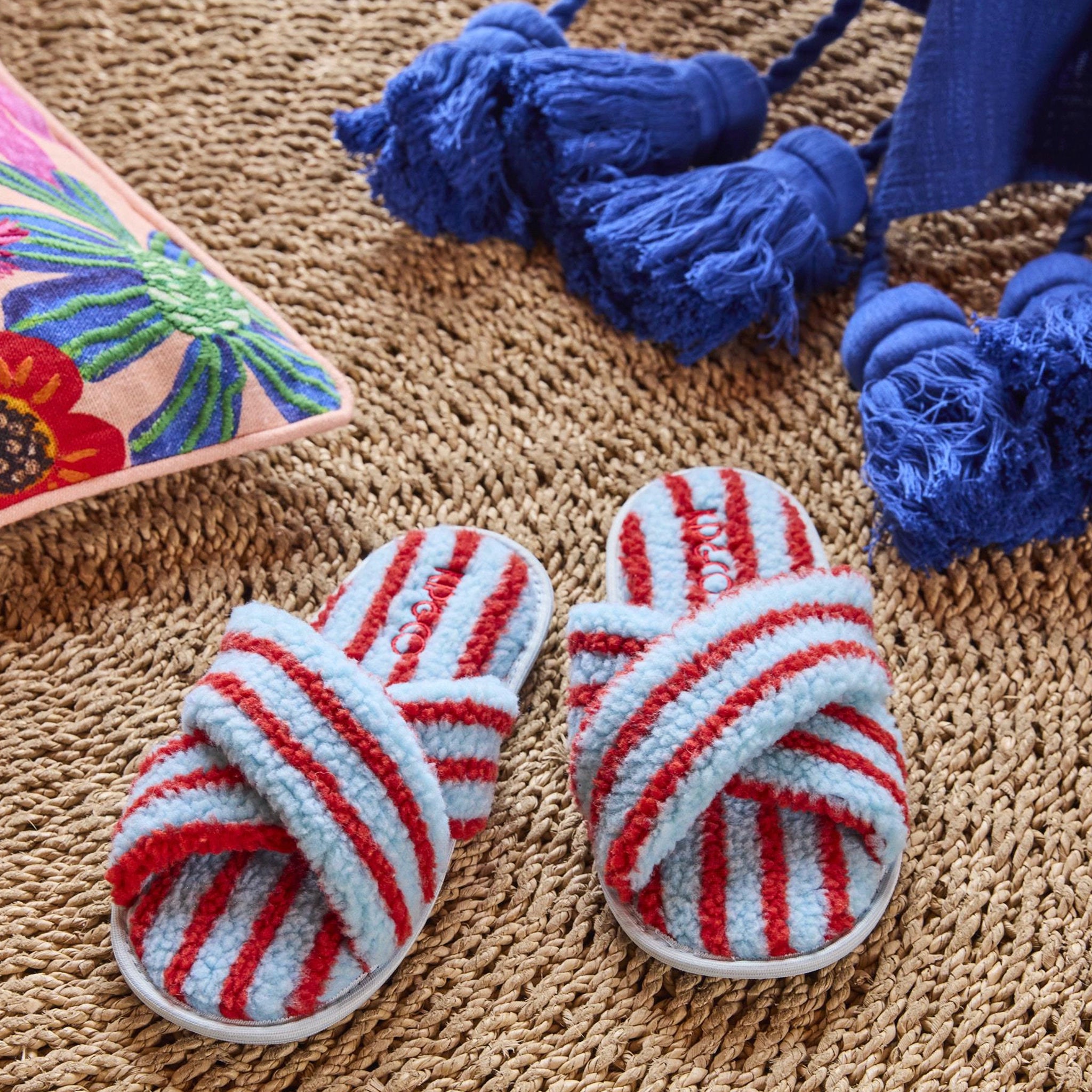 Pair of striped slippers on a textured surface with decorative tassels and a colorful pillow.