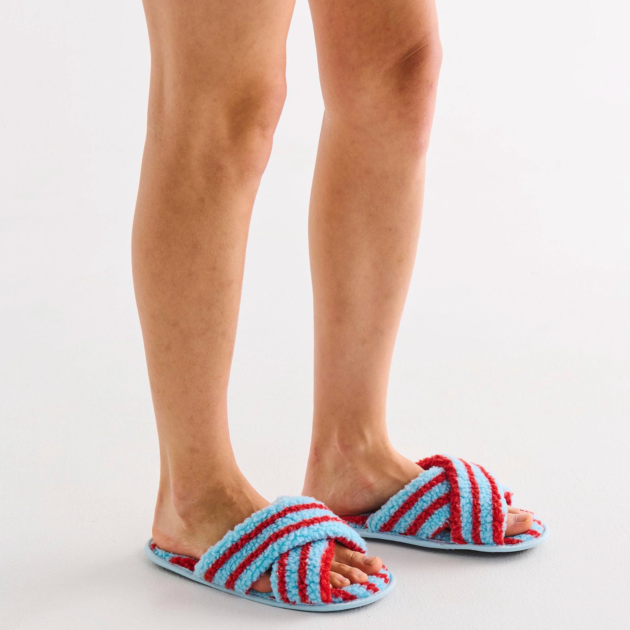 Striped blue and red slippers worn by a person on a light gray background