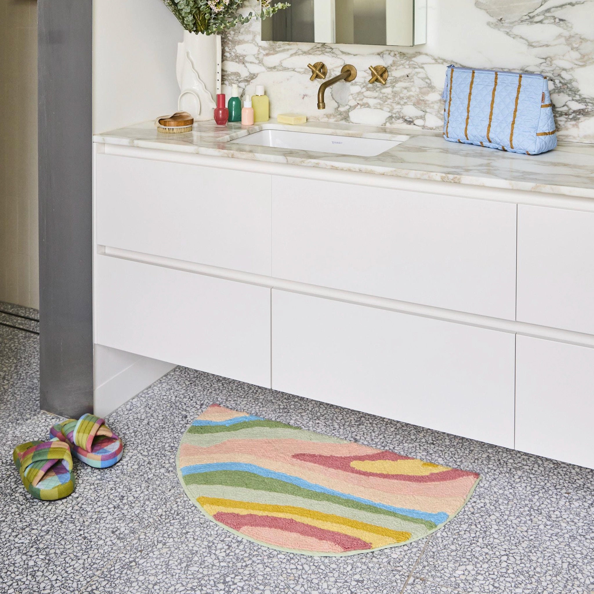 Bathroom with a colorful bath mat on the floor, sink, and striped towel.