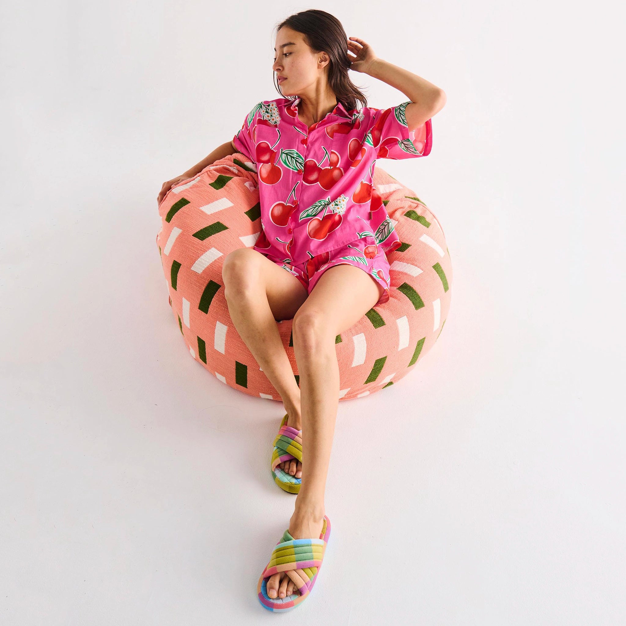 Woman in a pink cherry-themed outfit sitting on a colorful bean bag chair against a white background