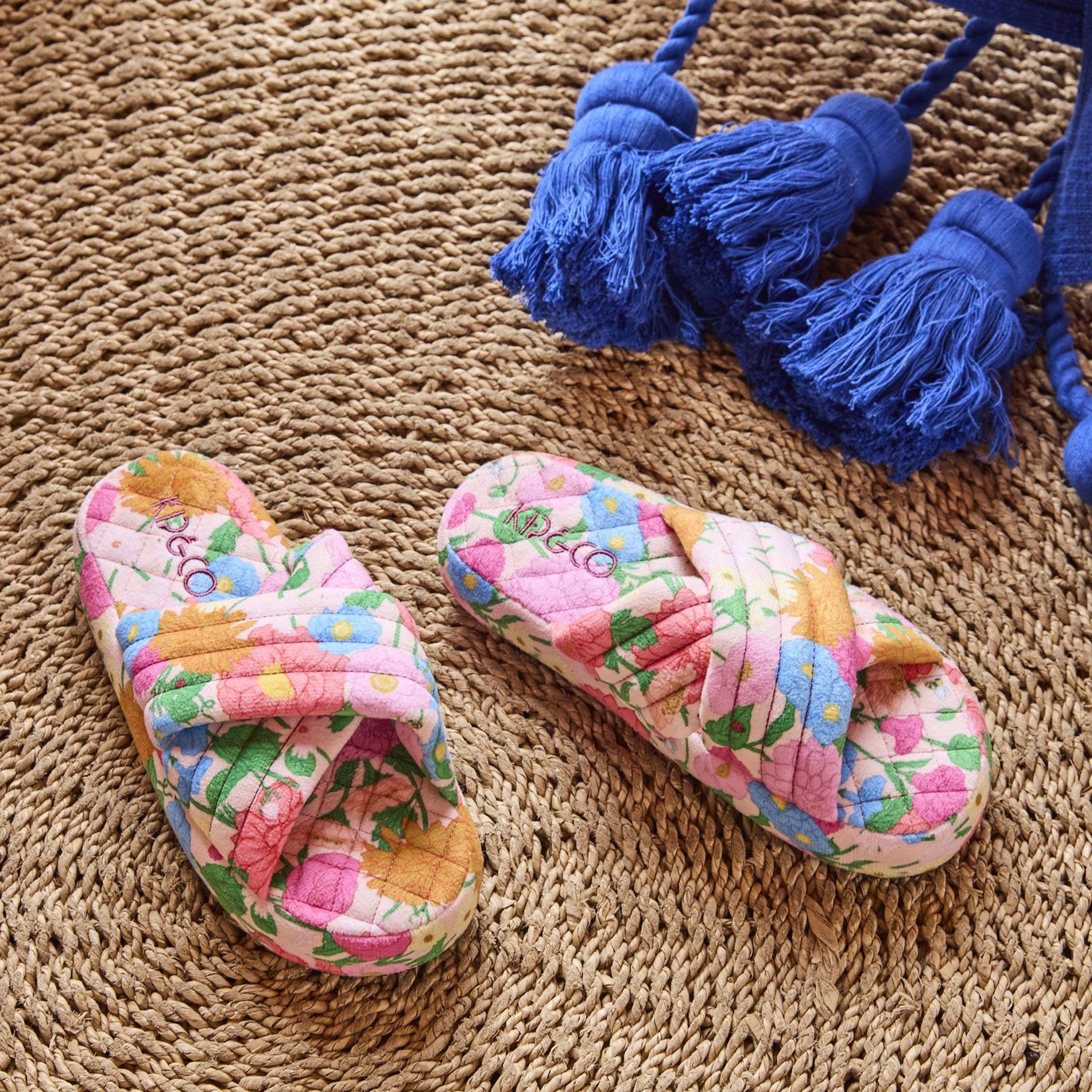 Pair of colorful floral slippers on a textured surface with blue tassels.