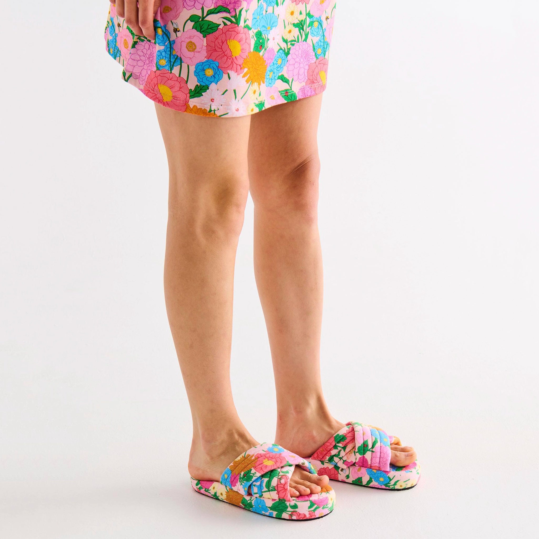 Person wearing colorful floral slippers and shorts on a white background