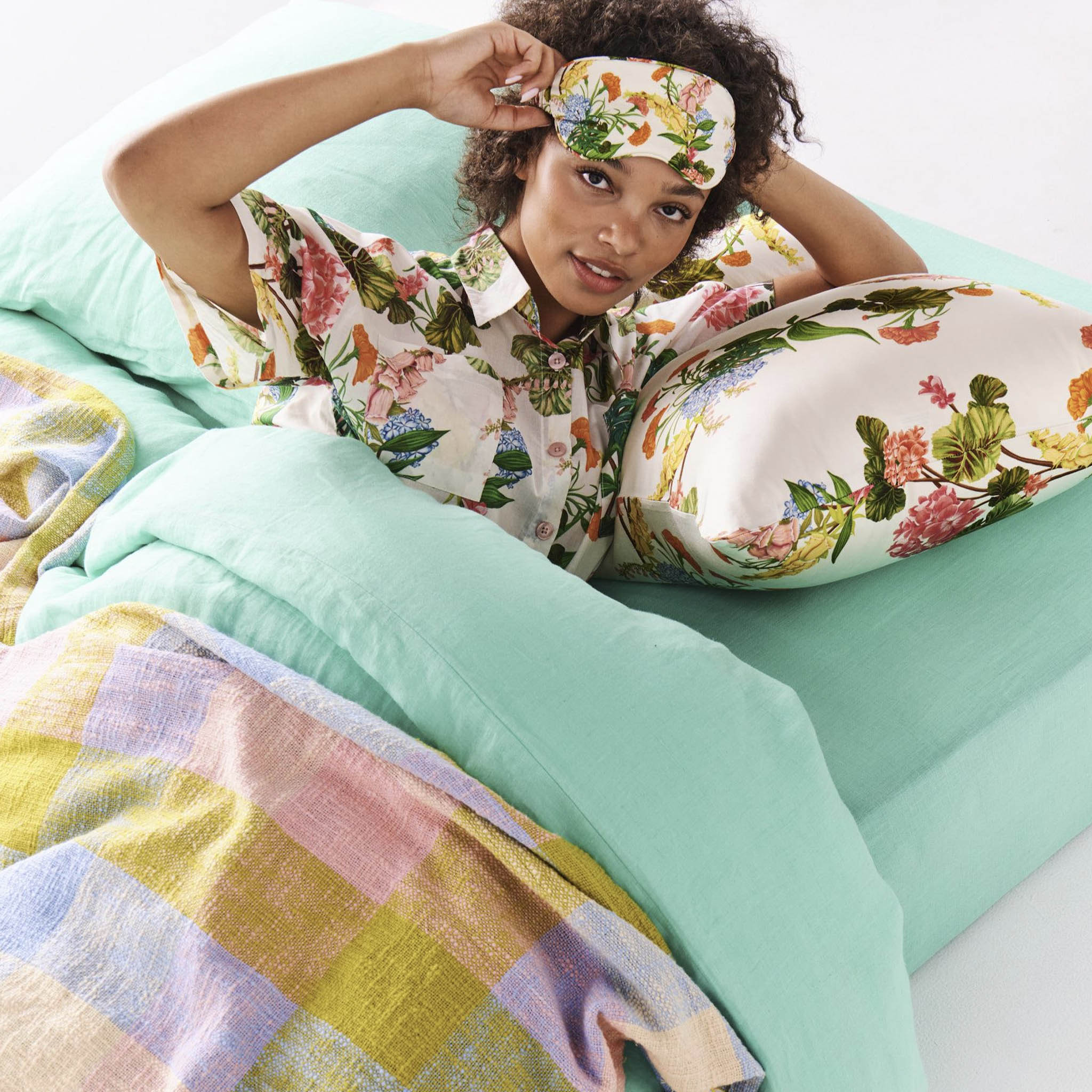 A woman in bed wearing a floral silk eye mask.