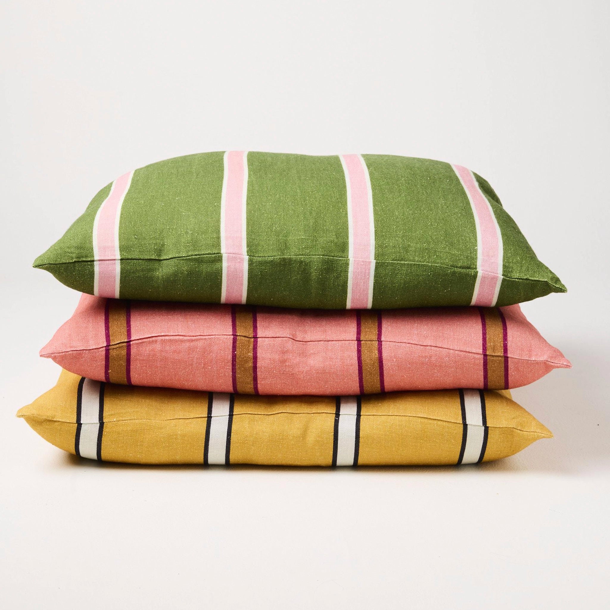 Stack of three striped cushions in green, pink, and yellow on a white background