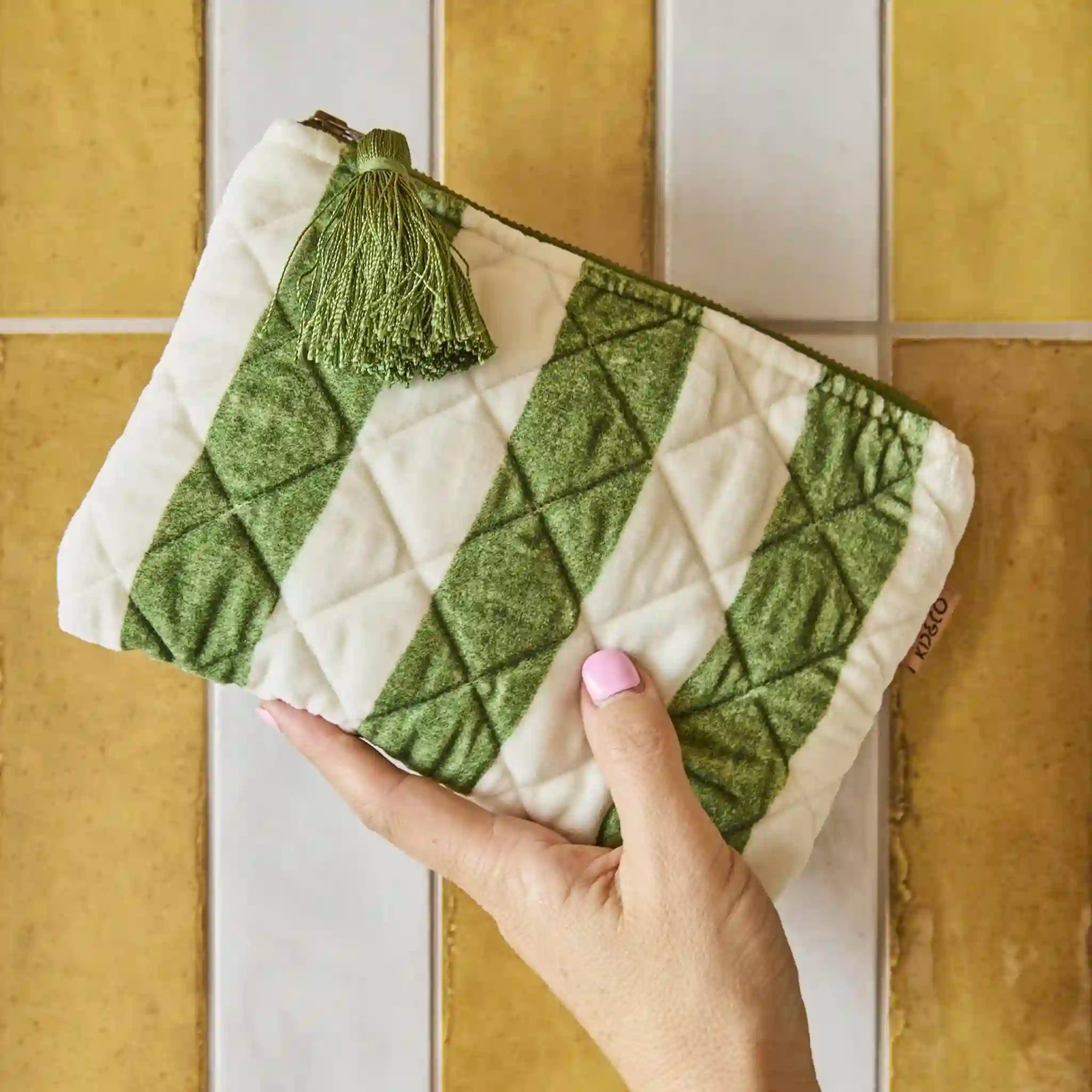 Green and white quilted cosmetic bag held by a hand against a tiled wall background