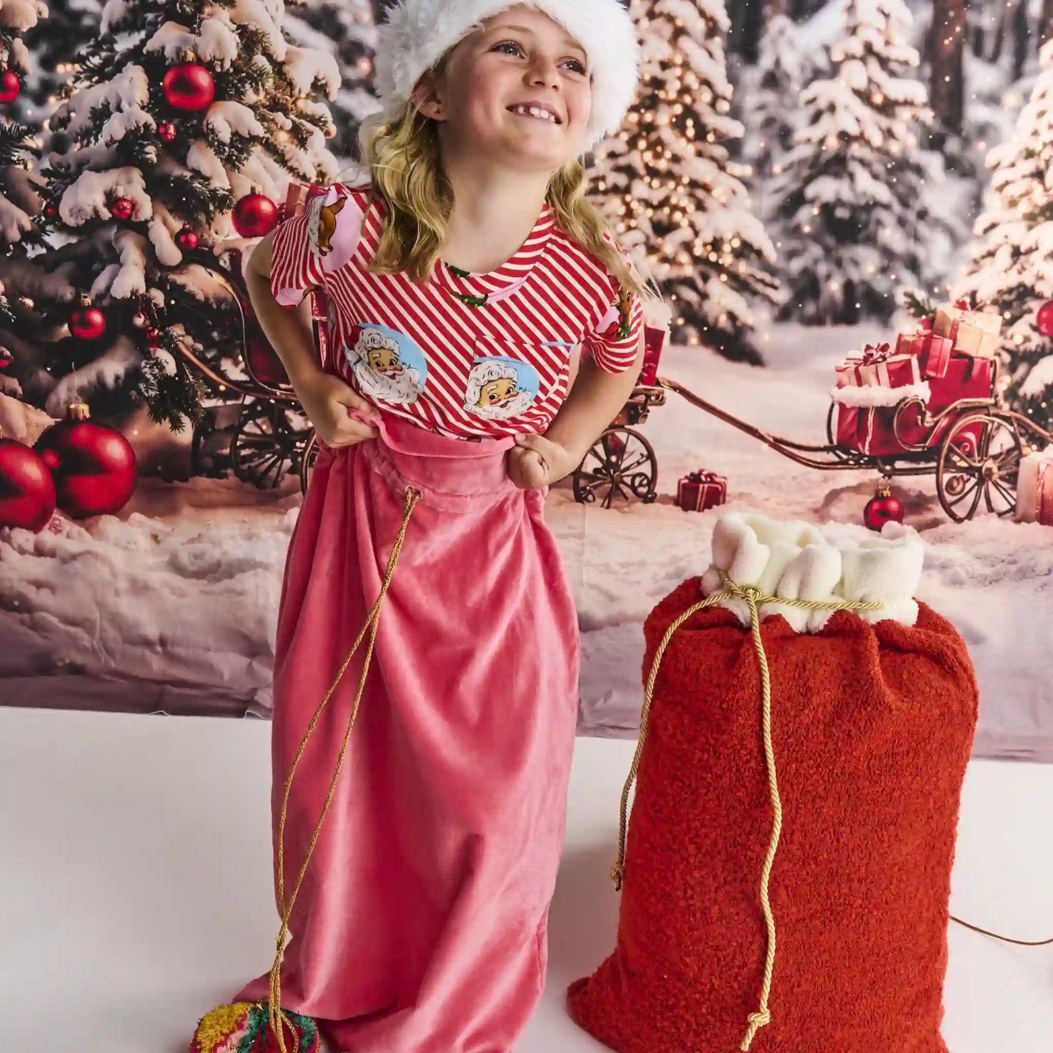 Young girl in a festive setting with Christmas decorations and a red sack.