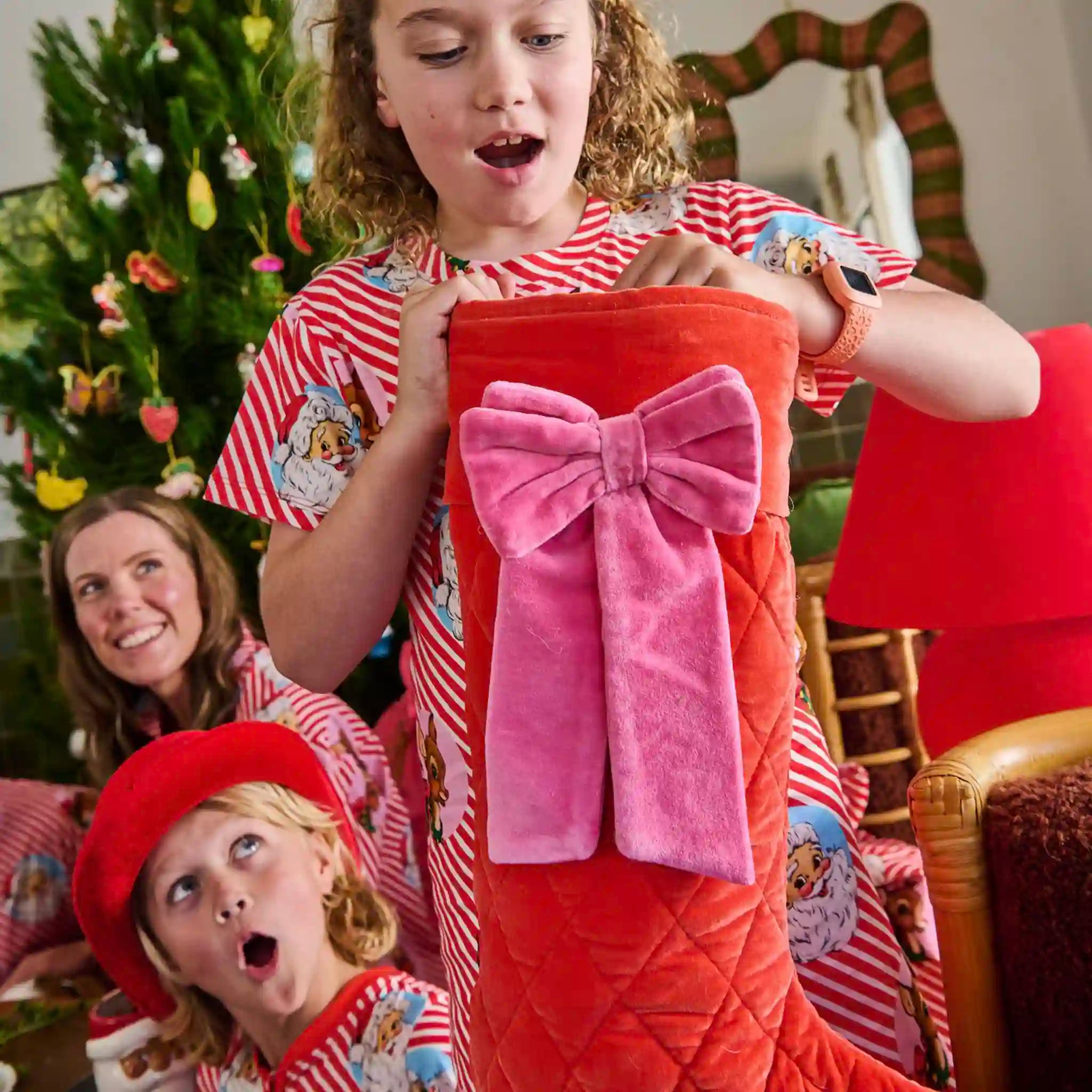 Children excitedly opening a large red gift bag with a pink bow in a festive setting.
