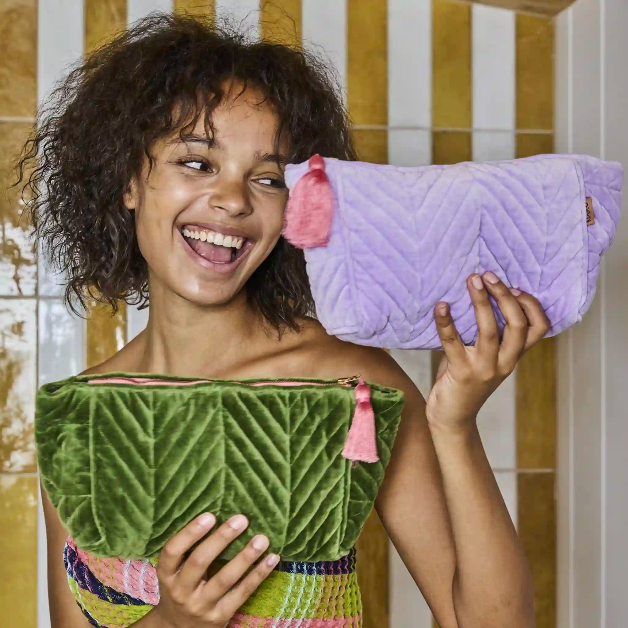 Child holding a green and purple quilted toiletry bag in a bathroom setting