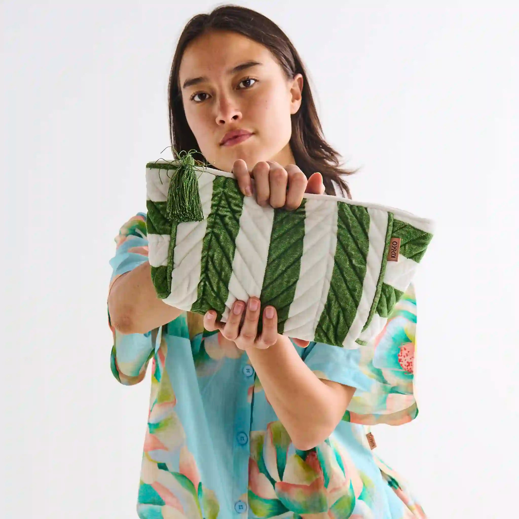 Woman holding a green and white patterned toiletry bag against a white background