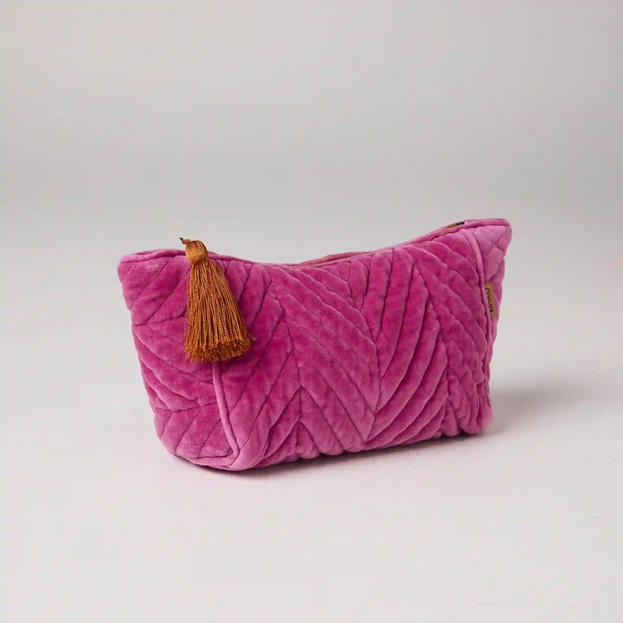 Pink textured toiletry bag with a tassel on a light gray background