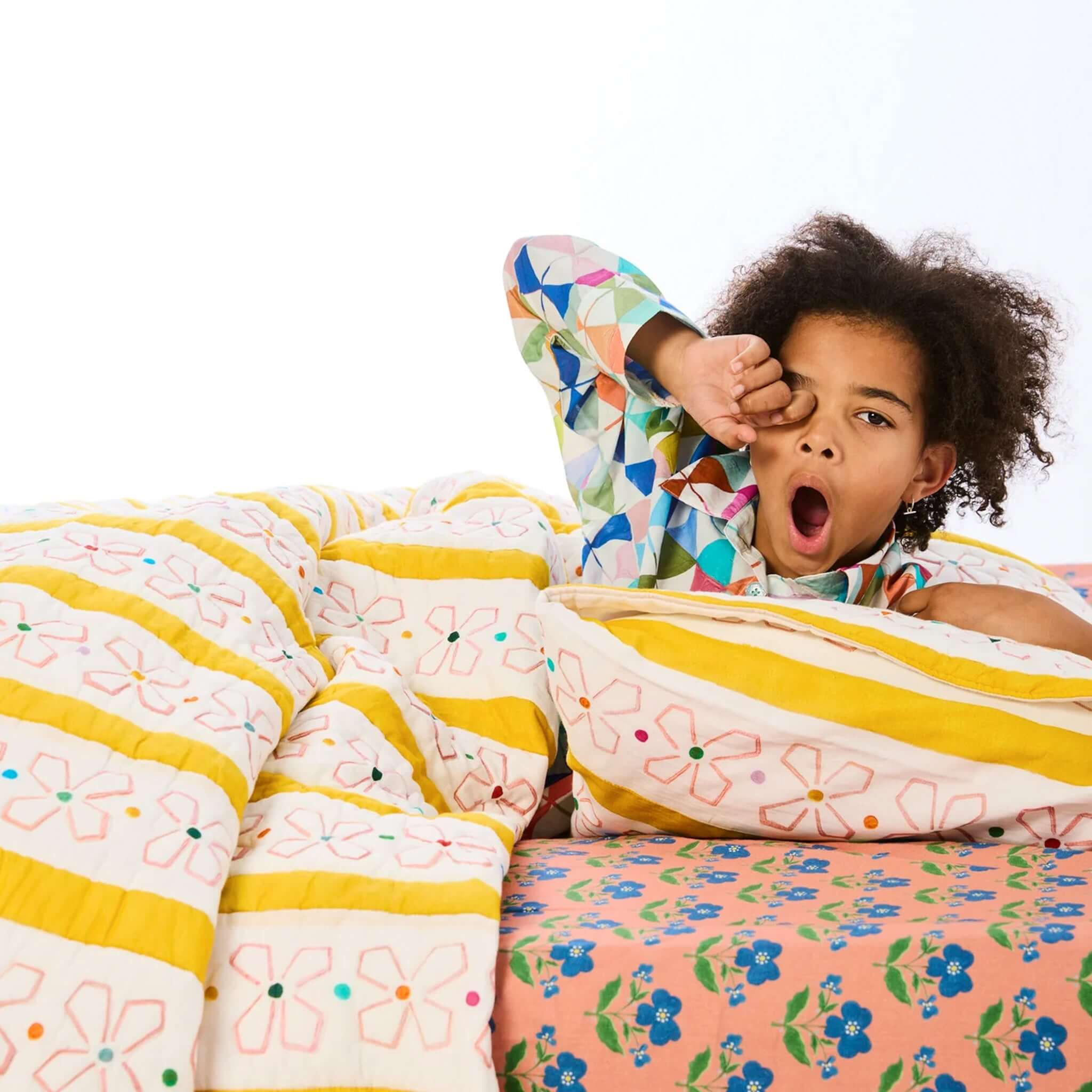 Kip & Co x Anna Spiro Daisy Chain Organic Cotton Quilted Bedspread - Single with child yawning in playful bedroom setting.