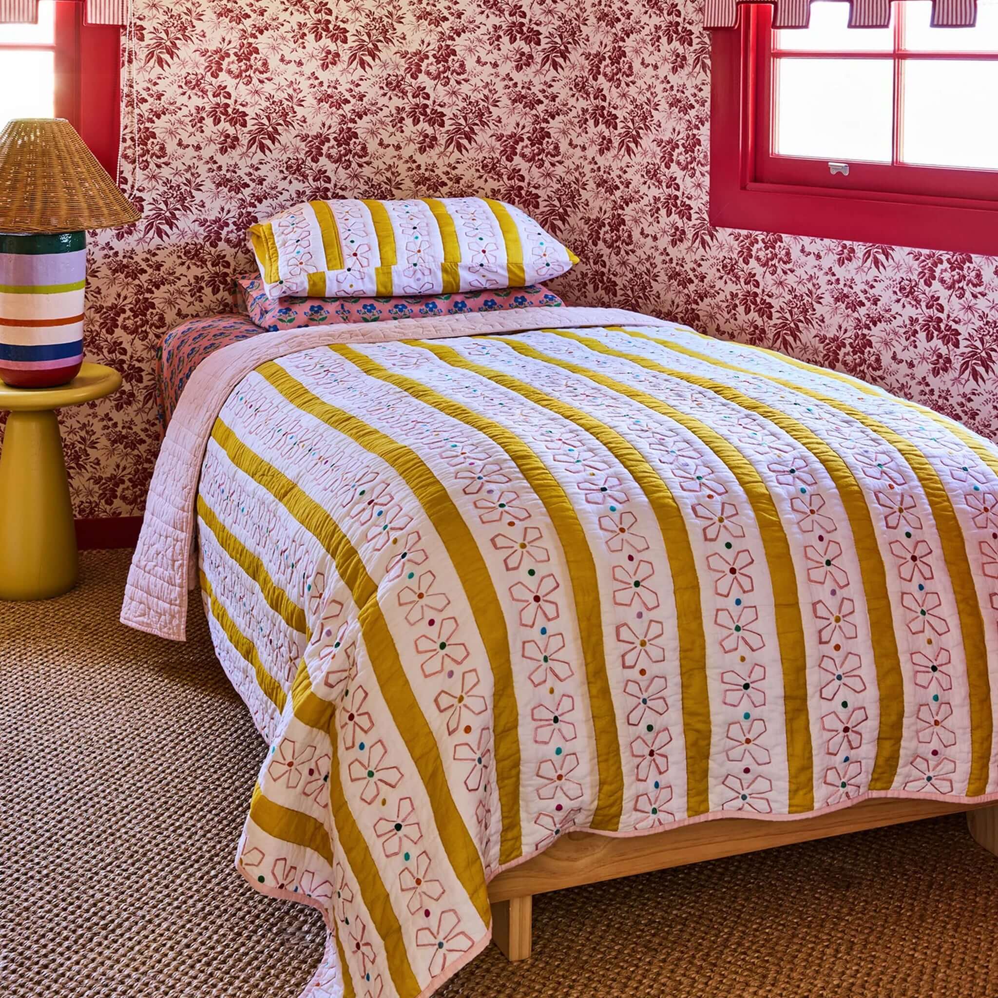 Kip & Co x Anna Spiro Daisy Chain Organic Cotton Quilted Pillowslip on a bed with floral wallpaper.