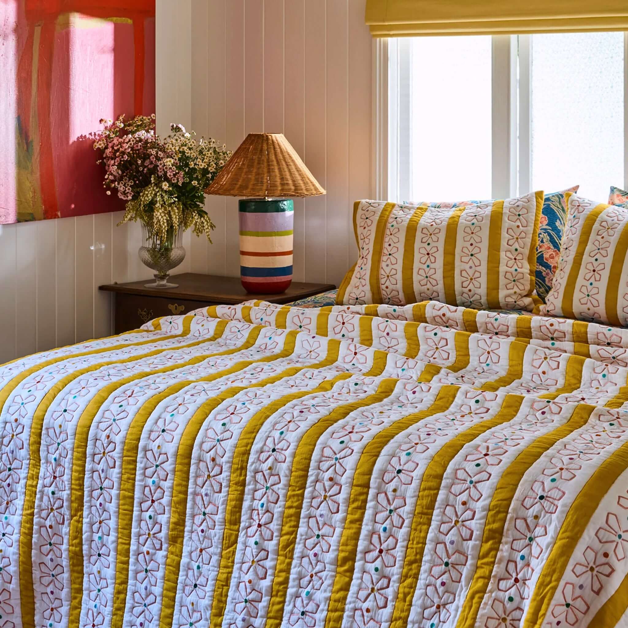 Kip & Co x Anna Spiro Daisy Chain Organic Cotton Quilted Pillowslip on a colorful bed with flowers and lamp.