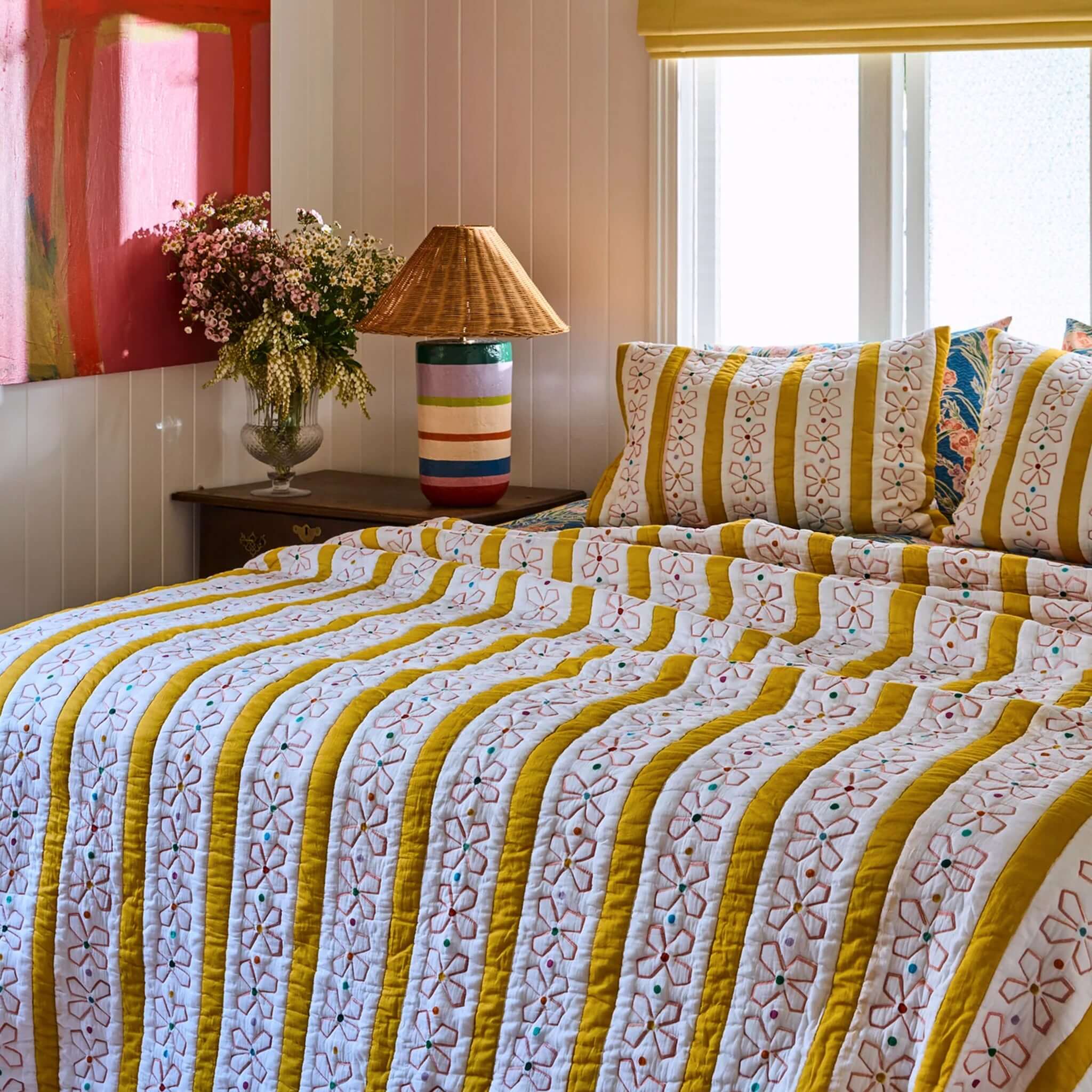 Kip & Co x Anna Spiro Daisy Chain Organic Cotton Quilted Bedspread - Large on a bed with floral and striped design.