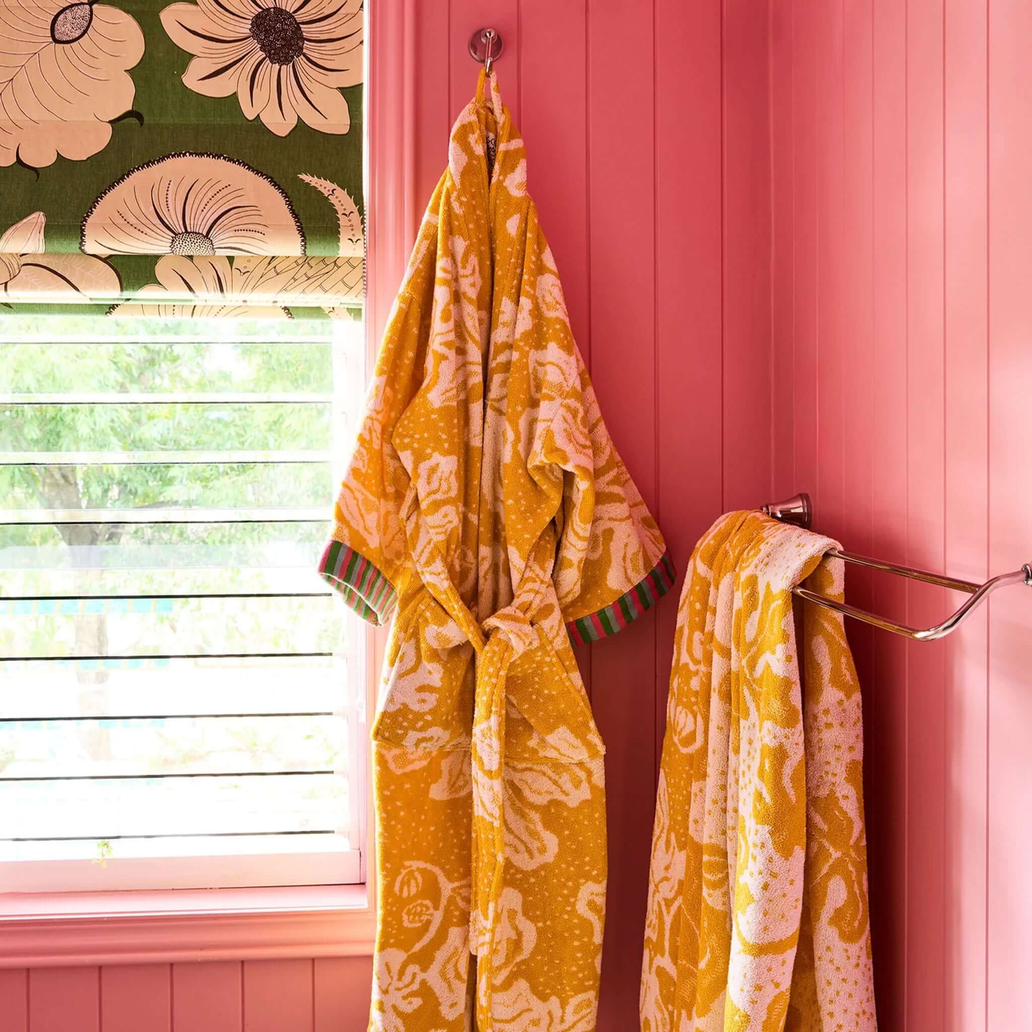 Kip & Co x Anna Spiro Elsternwig Fig Terry Bath Robe hanging in a vibrant pink bathroom with floral decor.