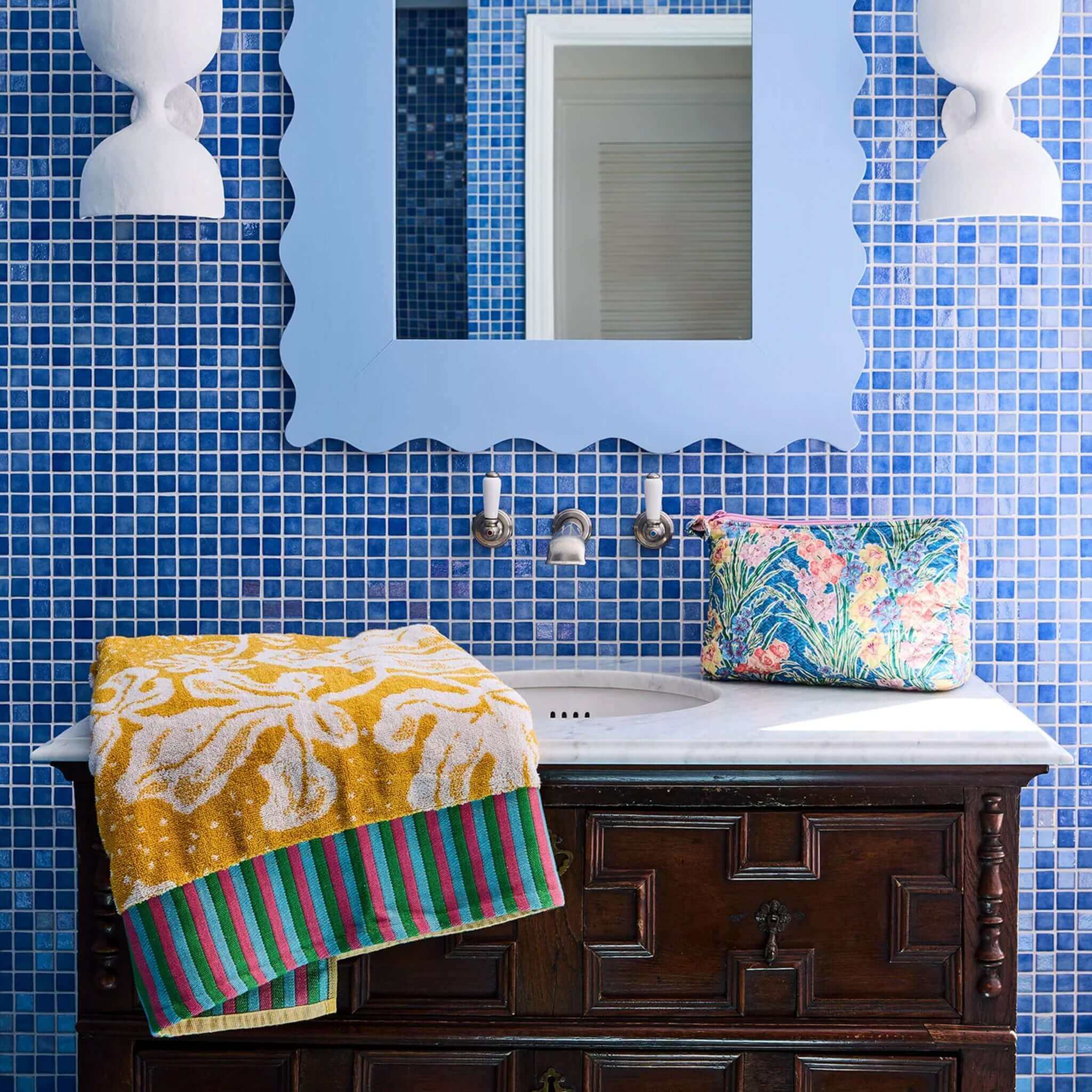 Kip & Co x Anna Spiro Elsternwig Fig Terry Face Washer draped over a marble sink in a vibrant blue tiled bathroom.