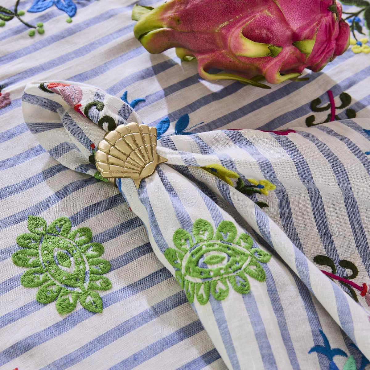 Kip & Co x Anna Spiro Malabar Floral embroidered linen close-up with a gold shell napkin ring and dragon fruit