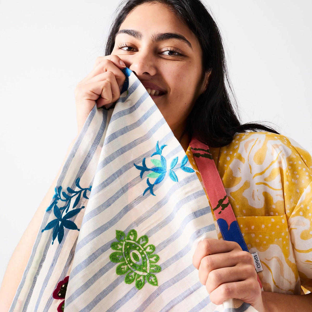 Kip & Co x Anna Spiro Embroidered Linen Napkin - Malabar Floral held up by a model in a yellow shirt