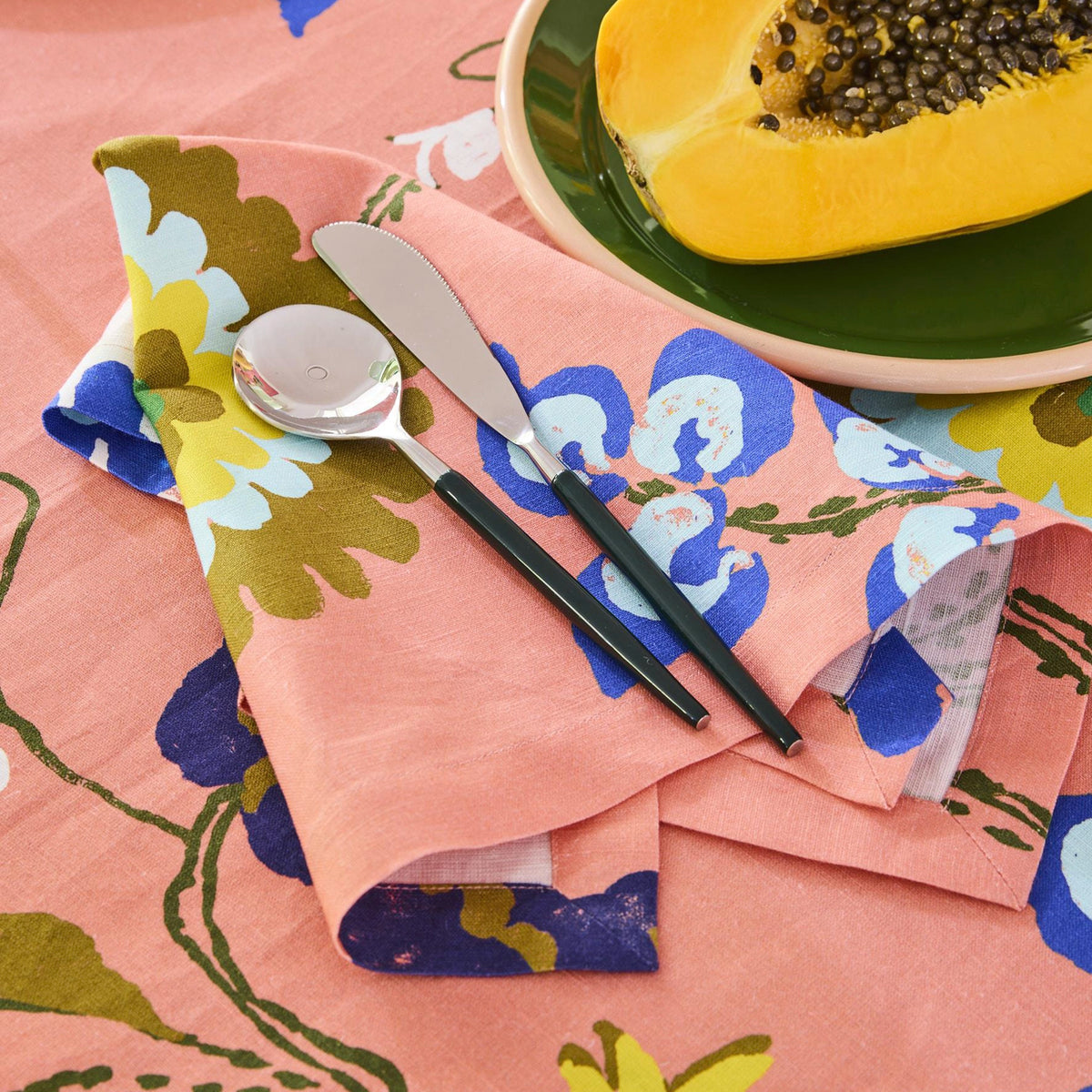 Kip & Co x Anna Spiro Isabelle Sunset linen close-up with cutlery and a bowl of papaya on the coral floral print