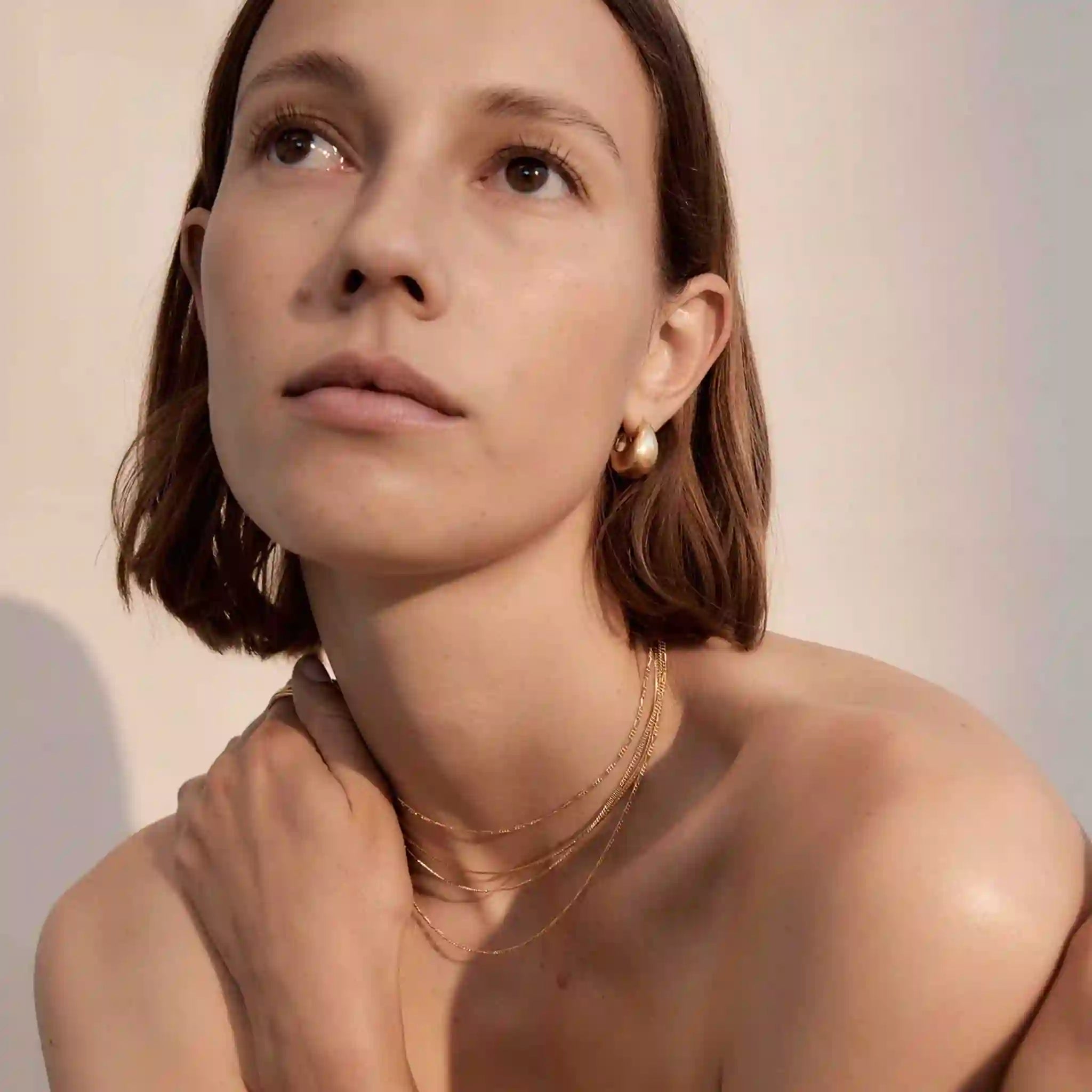 Woman wearing gold necklaces and earrings against a neutral background