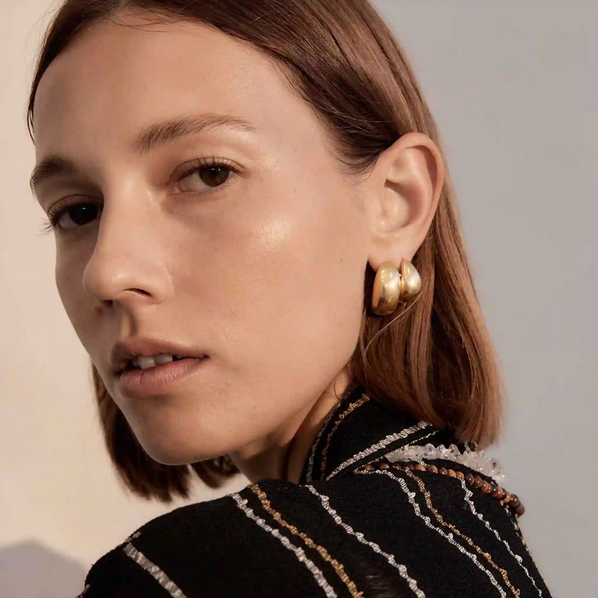 Close-up of a woman wearing gold earrings with a neutral background