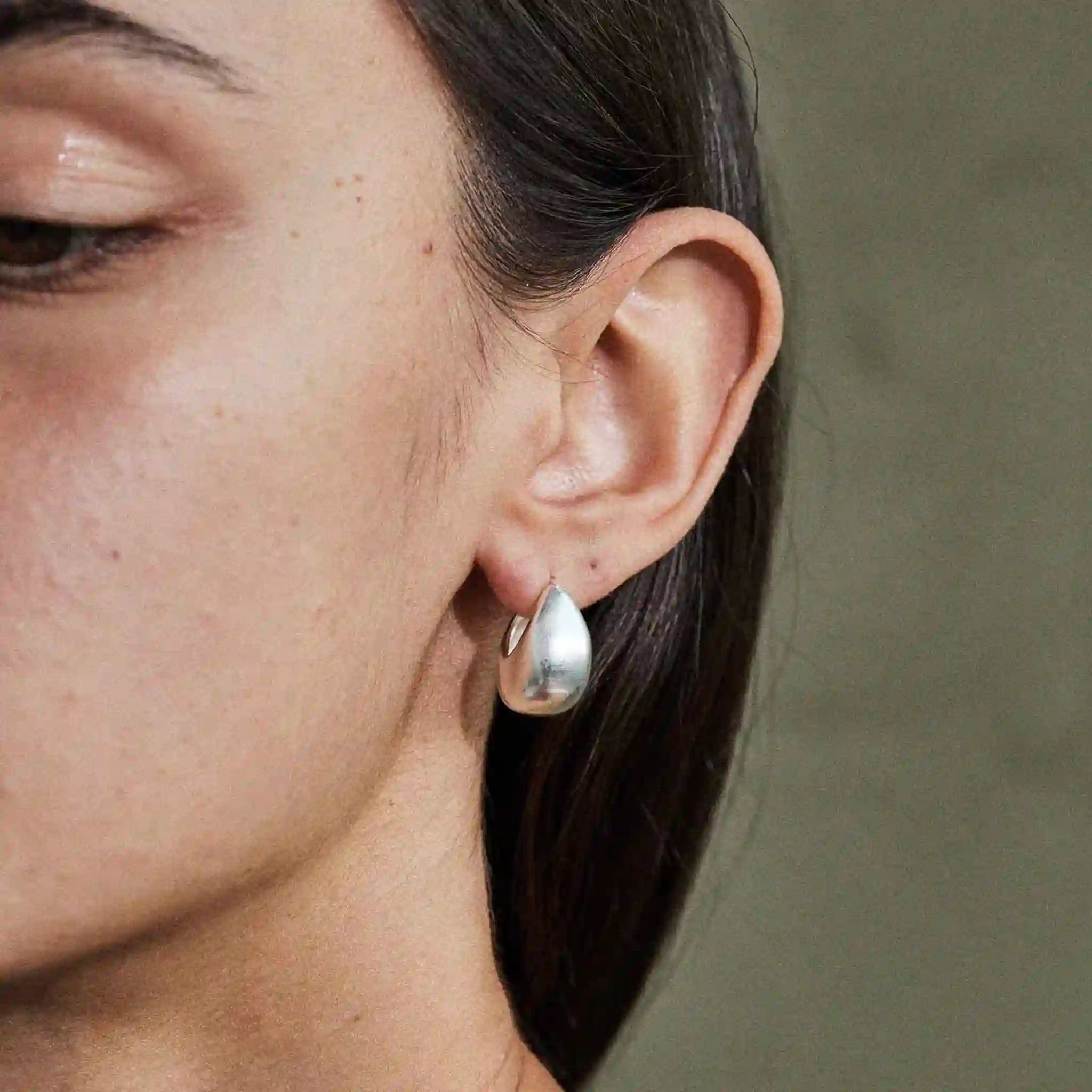 Close-up of a person wearing a silver teardrop earring against a neutral background